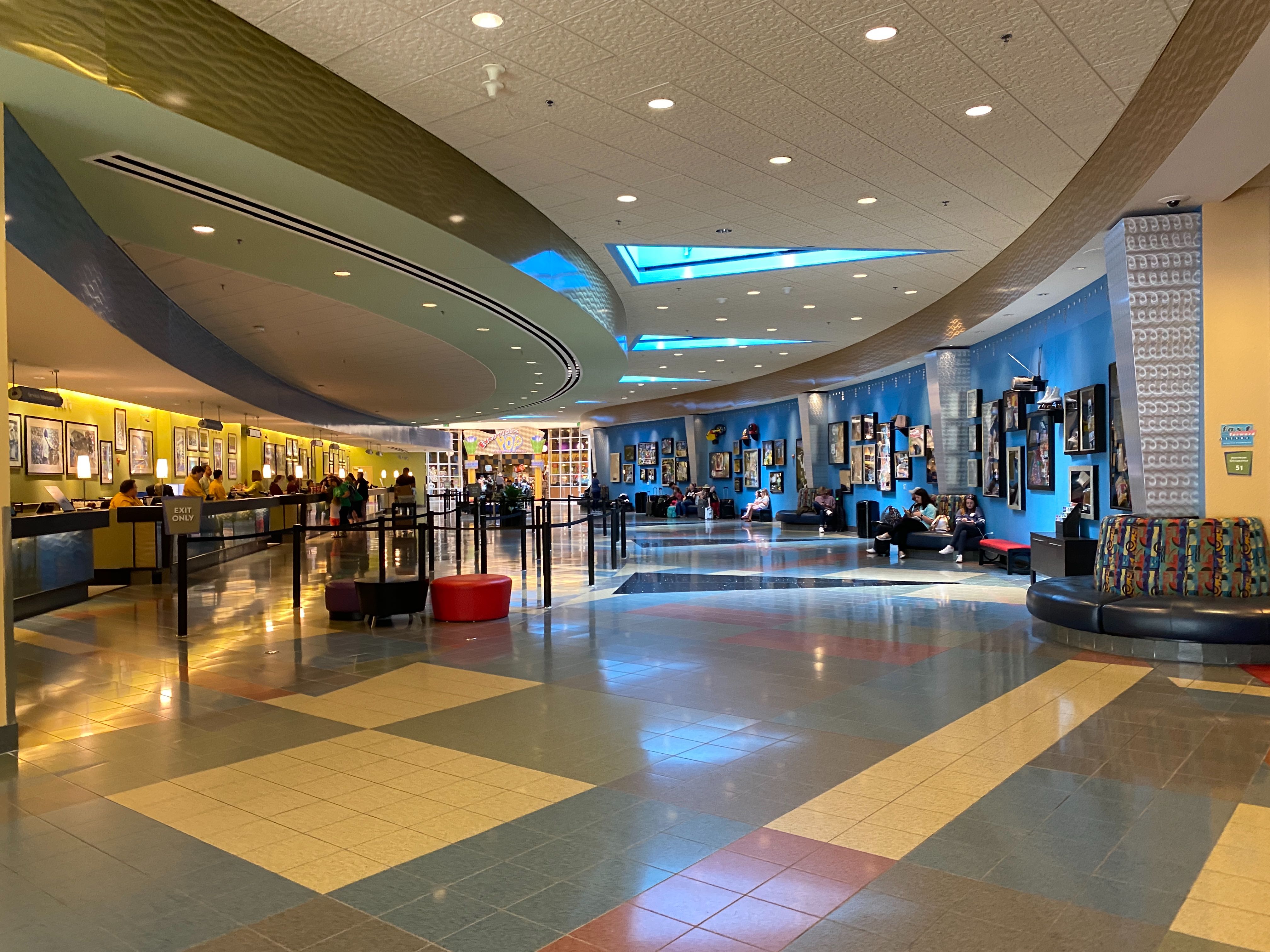 Curved lobby of Disney's Pop Century Resort with alternating colored tiles, triangular skylights, and a blue wall of display cases.