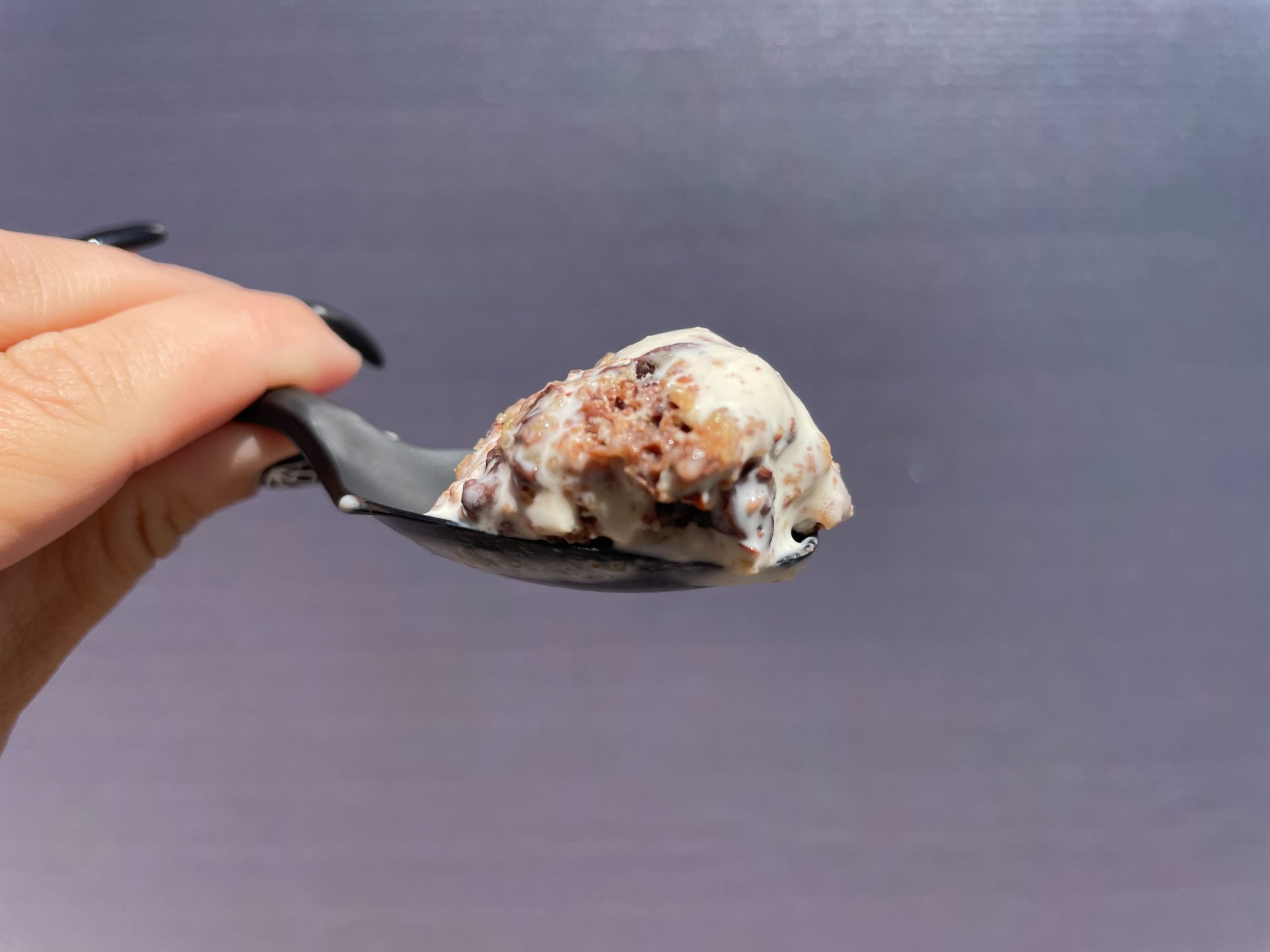 Spoon with a bite of Salt & Straw ice cream cup with a scoop of The Great Candycopia salted butterscotch ice cream with chocolate candy pieces.
