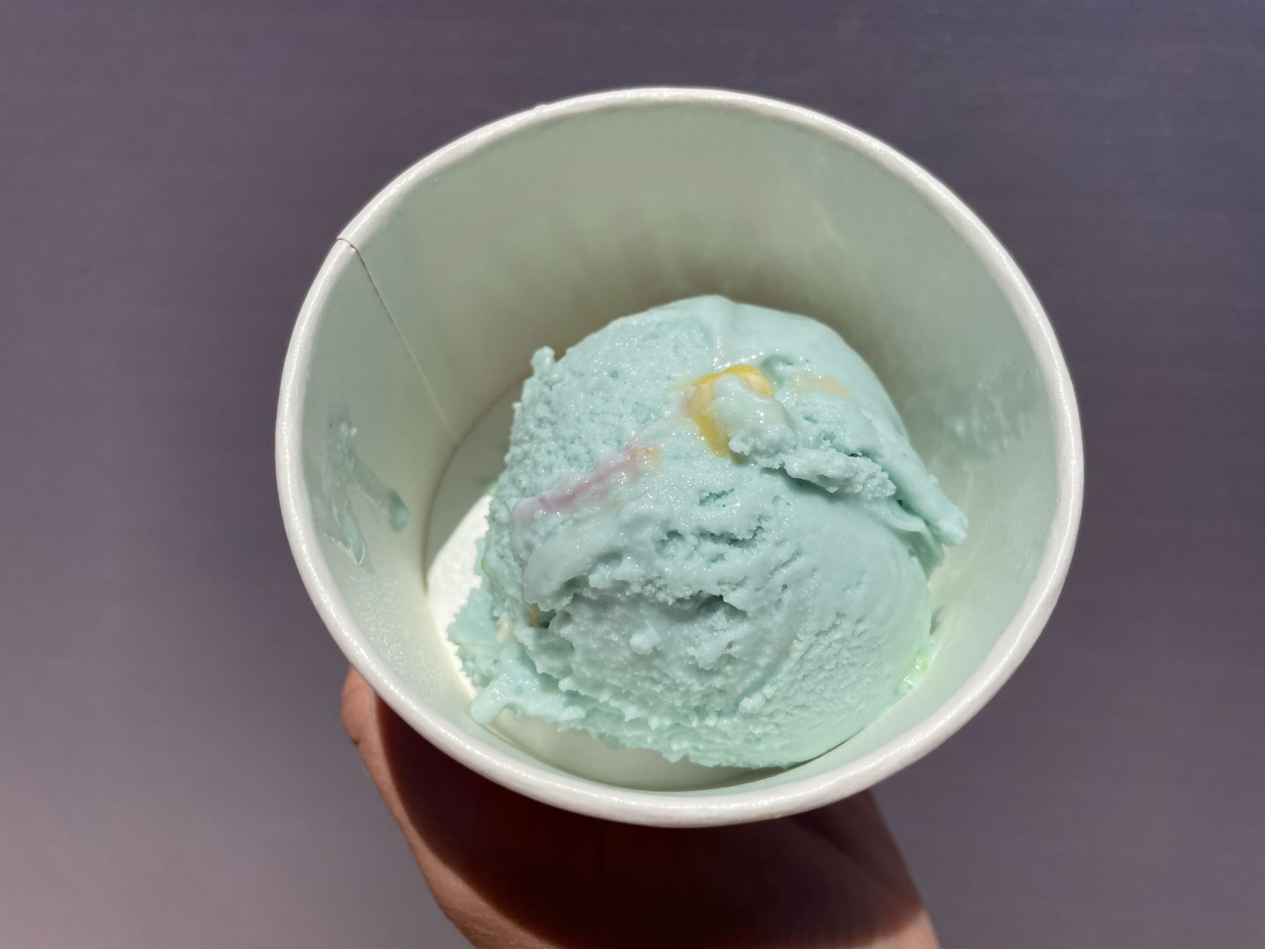 Hand holding a Salt & Straw ice cream cup with a scoop of light blue Double Bubble Toil and Trouble vegan bubblegum ice cream.