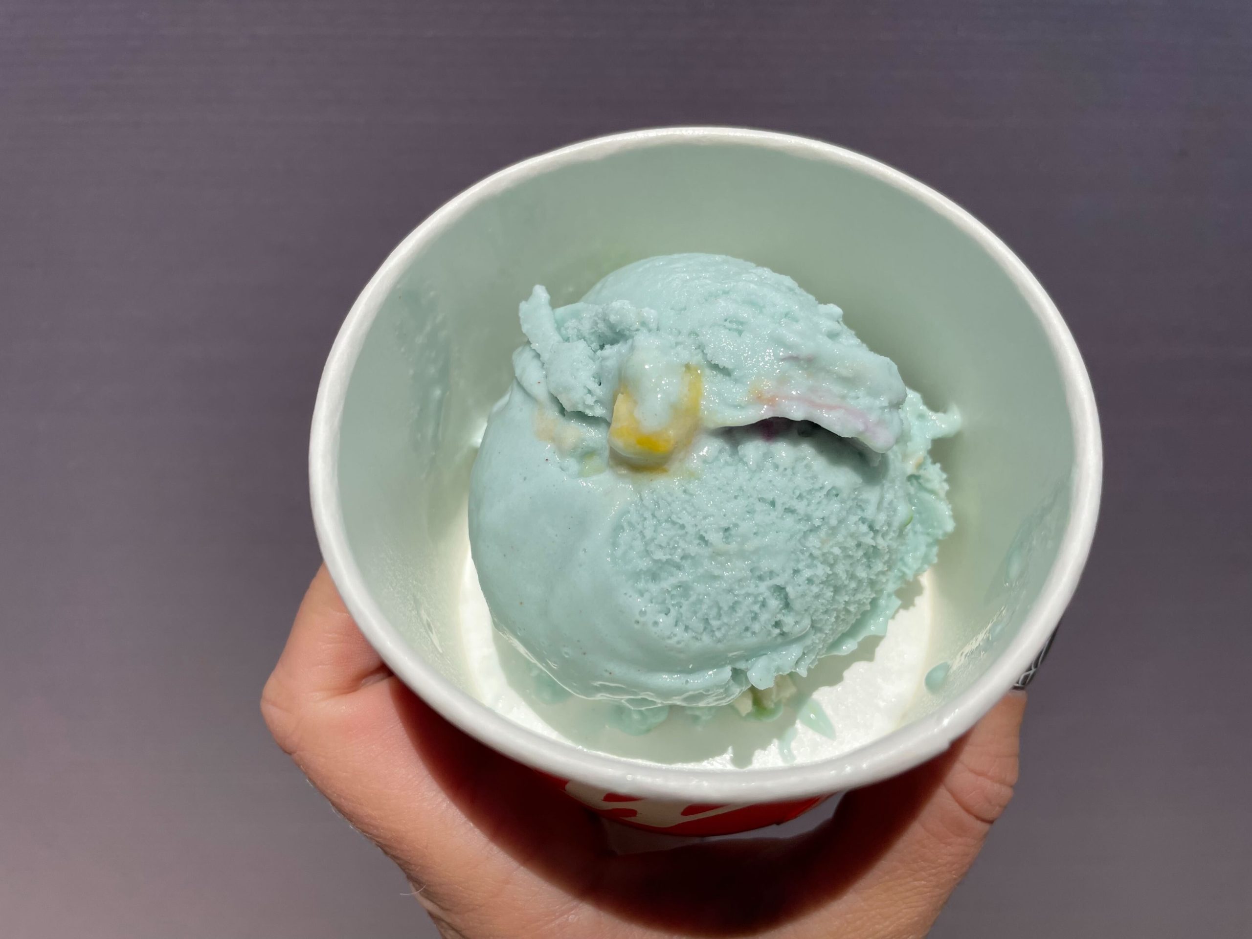 Hand holding a Salt & Straw ice cream cup with a scoop of light blue Double Bubble Toil and Trouble vegan bubblegum ice cream.