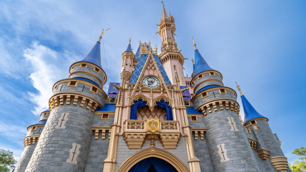 A tall, ornate castle with blue spires and clock on the main tower set against a blue sky.