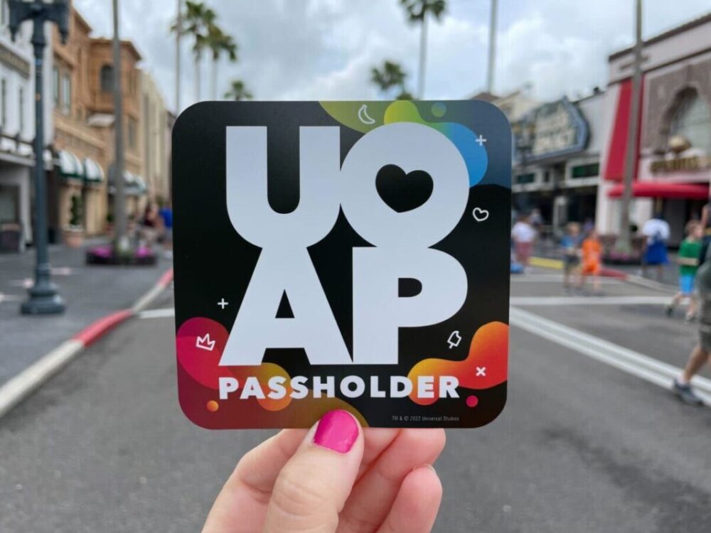 Amid a bustling backdrop of shops and lively visitors, a proud Universal Orlando Annual Passholder showcases their sticker, capturing the excitement of endless adventures.