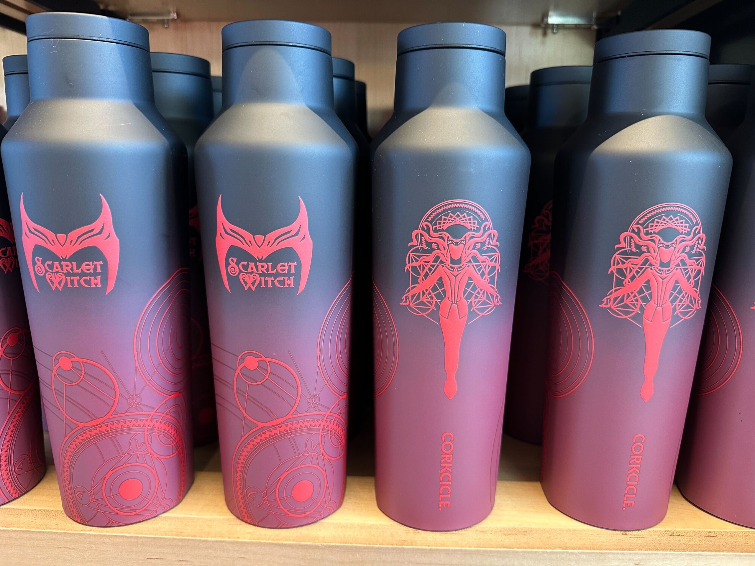 Several black and red insulated bottles featuring Scarlet Witch designs and the Corkcicle brand name are displayed on a shelf, each showcasing the mystique of the Marvel universe.