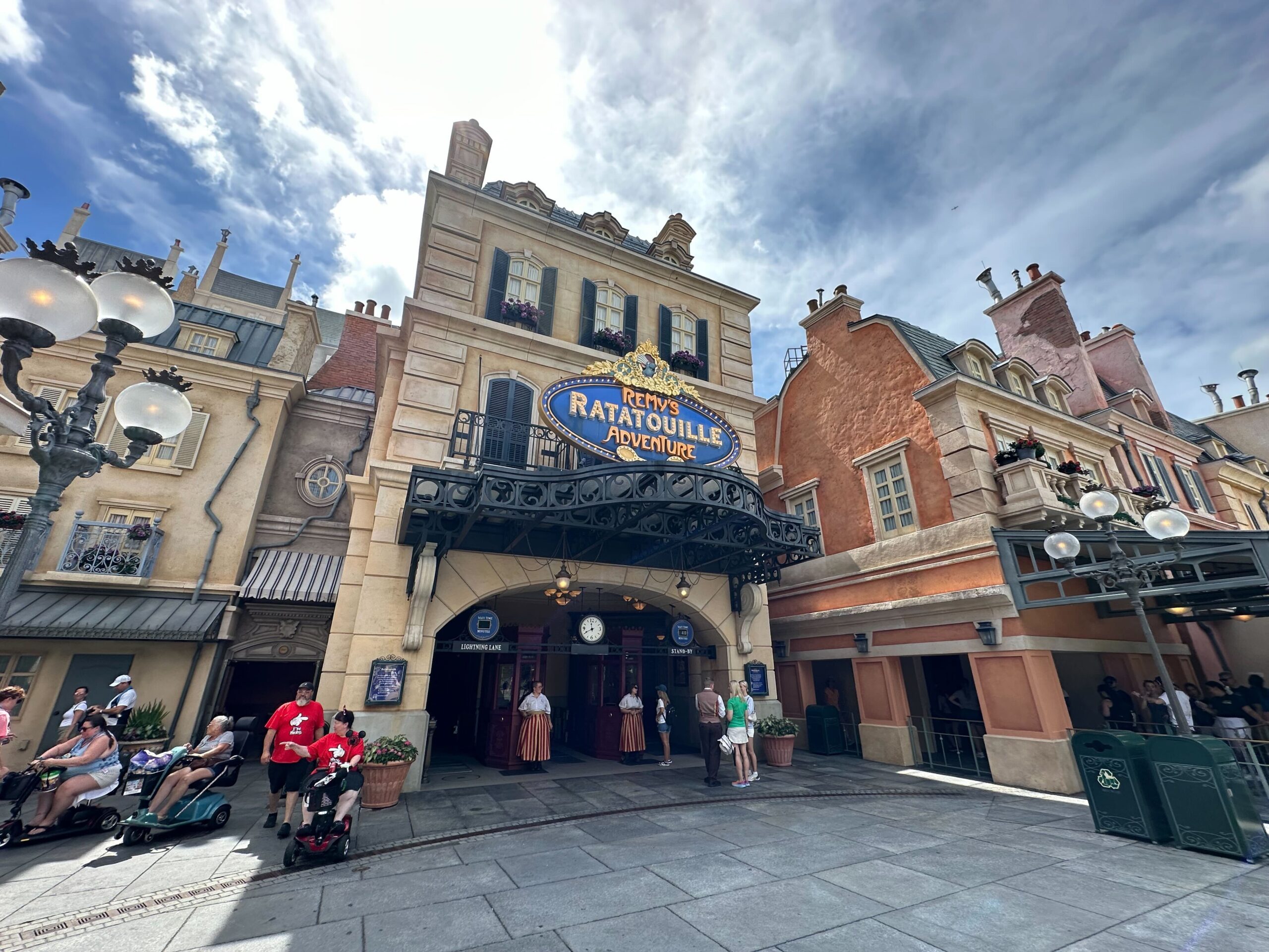 People walking in front of the entrance to Remy's Ratatouille Adventure, a themed attraction with a Parisian-style facade under a cloudy sky.