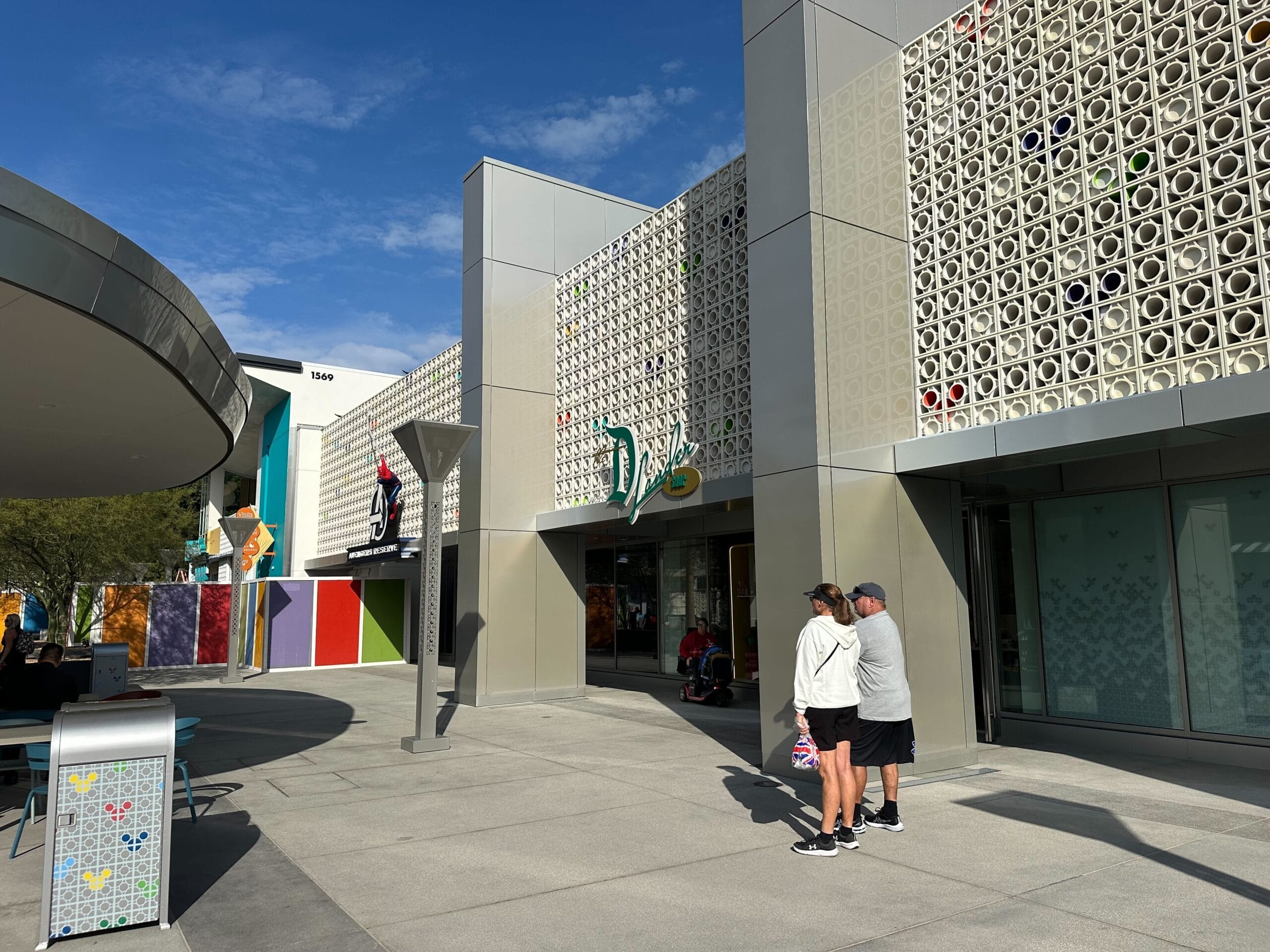 People stand outside a modern building with geometric patterns, under a clear blue sky.