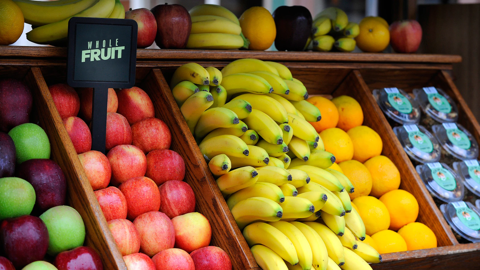 Wooden fruit cart on Main Street displaying apples, bananas, lemons, and packaged fruit with a "WHOLE FRUIT" sign.