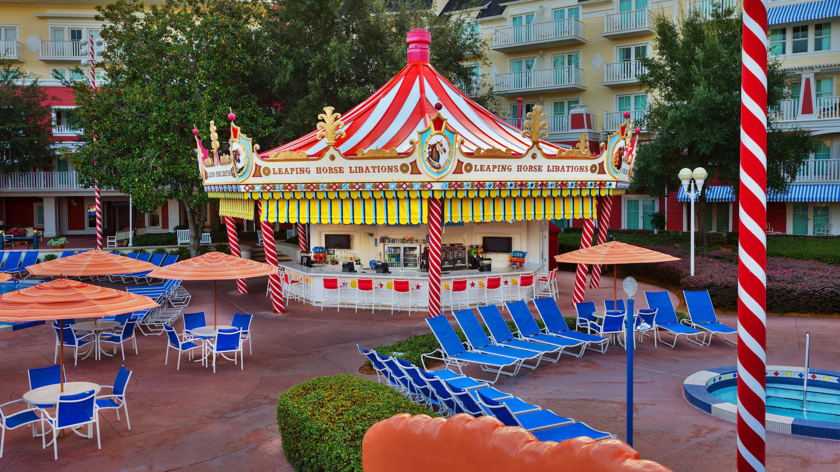 Colorful Leaping Horse Libations snack stand with a carousel-style roof, blue lounge chairs, and orange striped umbrellas.
