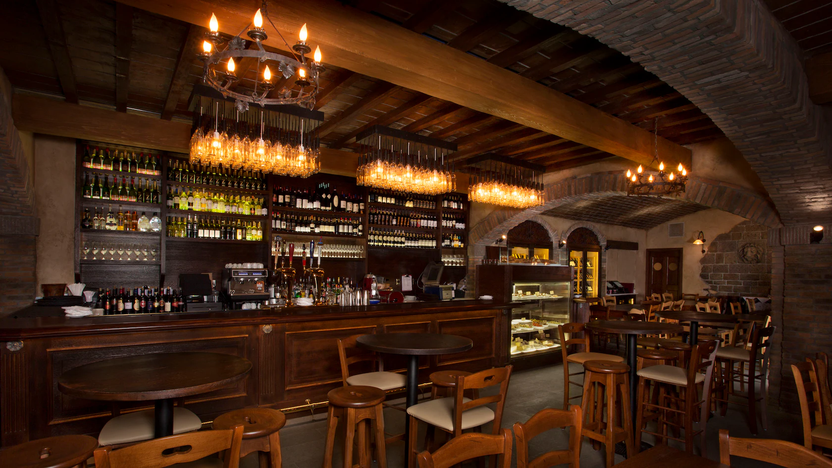 Cozy, rustic bar with wooden tables, chandeliers, and an Italian wine cellar stocked behind the counter.