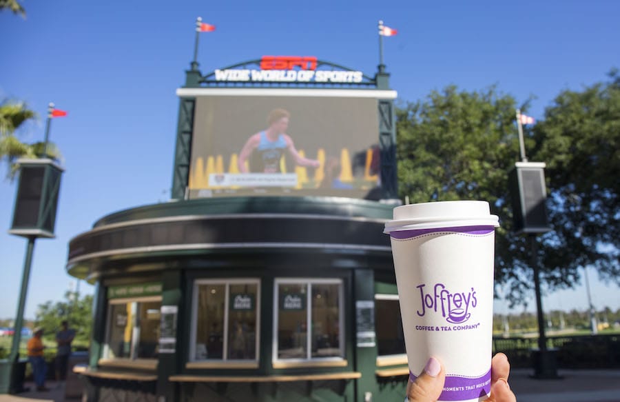 Hand holding a Joffrey’s Coffee & Tea Company cup at Wide World of Sports with a large screen in the background.