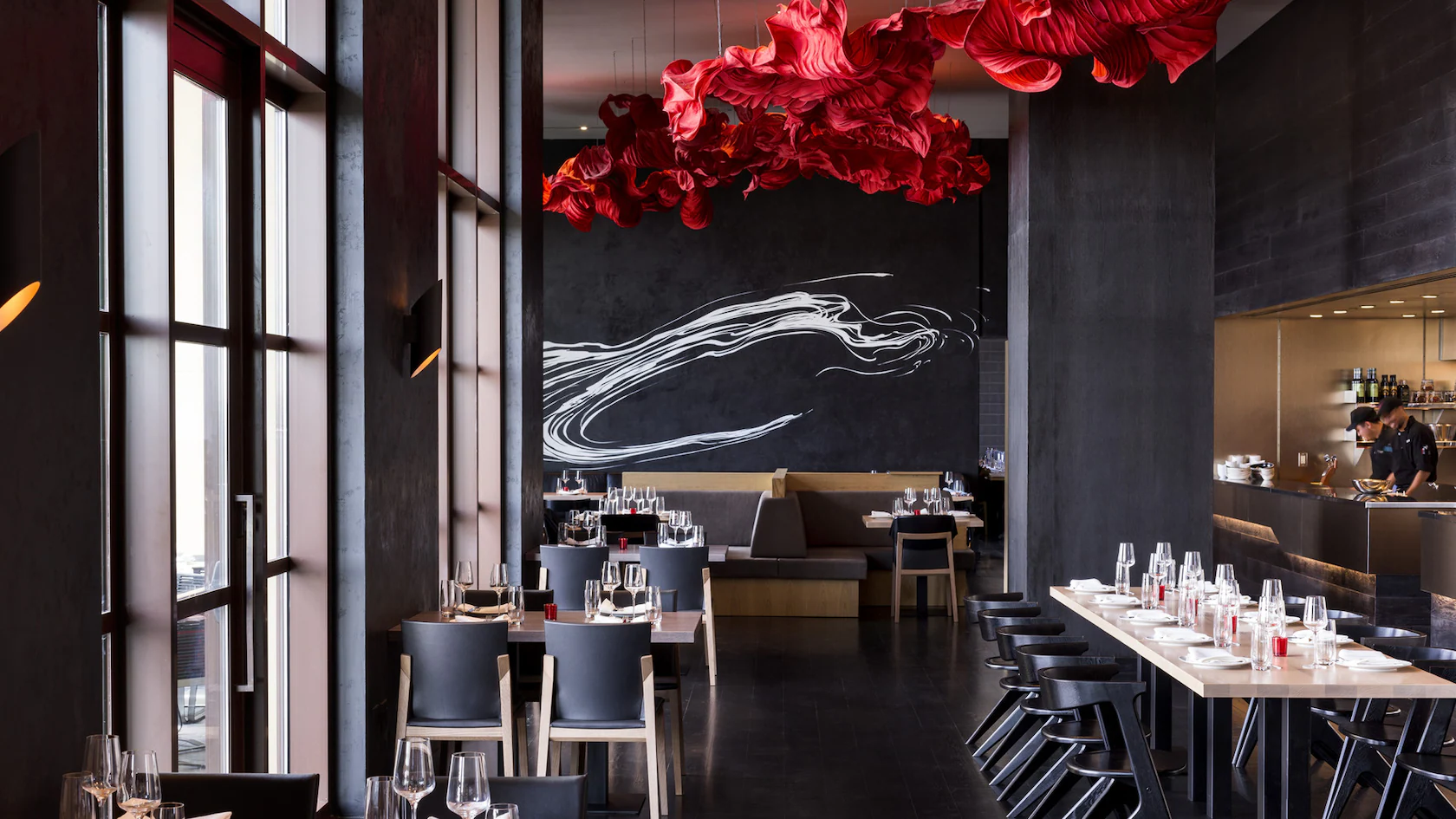 Modern restaurant with black walls, red abstract ceiling decor, and tables set with glasses and white napkins.
