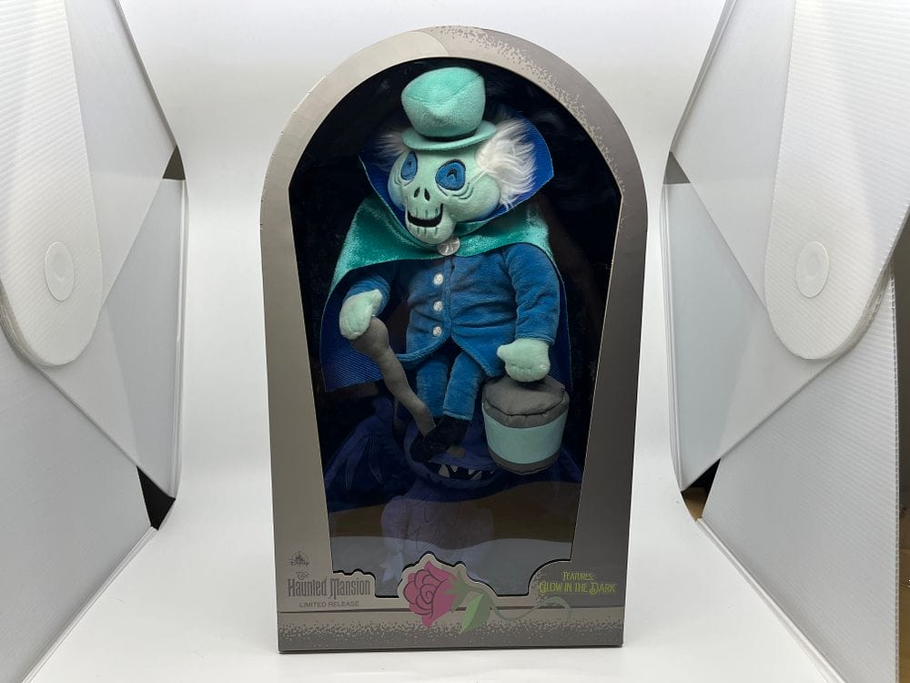 Haunted Mansion limited edition figure in packaging from the WDWNT Spring Cleaning Auction 2025. Features a skeleton in a blue coat and hat, holding a hatbox. Packaging adorned with a rose and glow-in-the-dark label.