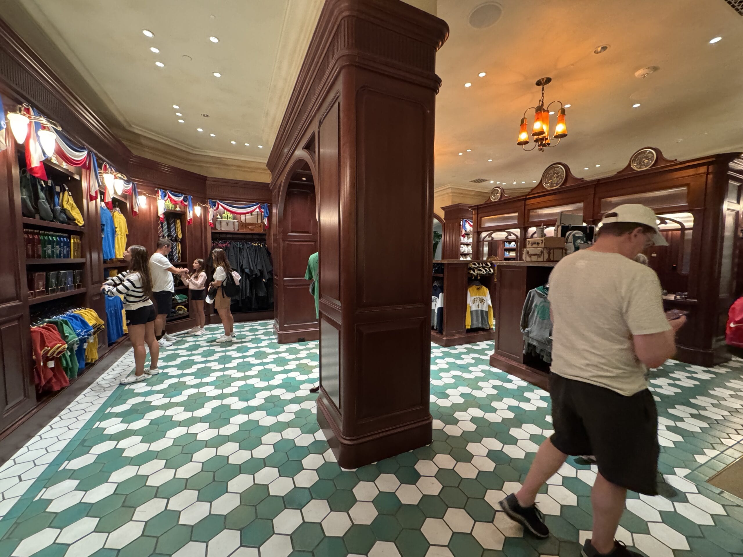 People shopping for clothes in a store with green and white hexagonal tile floor at Epic Universe’s Tour En Floo Shop.