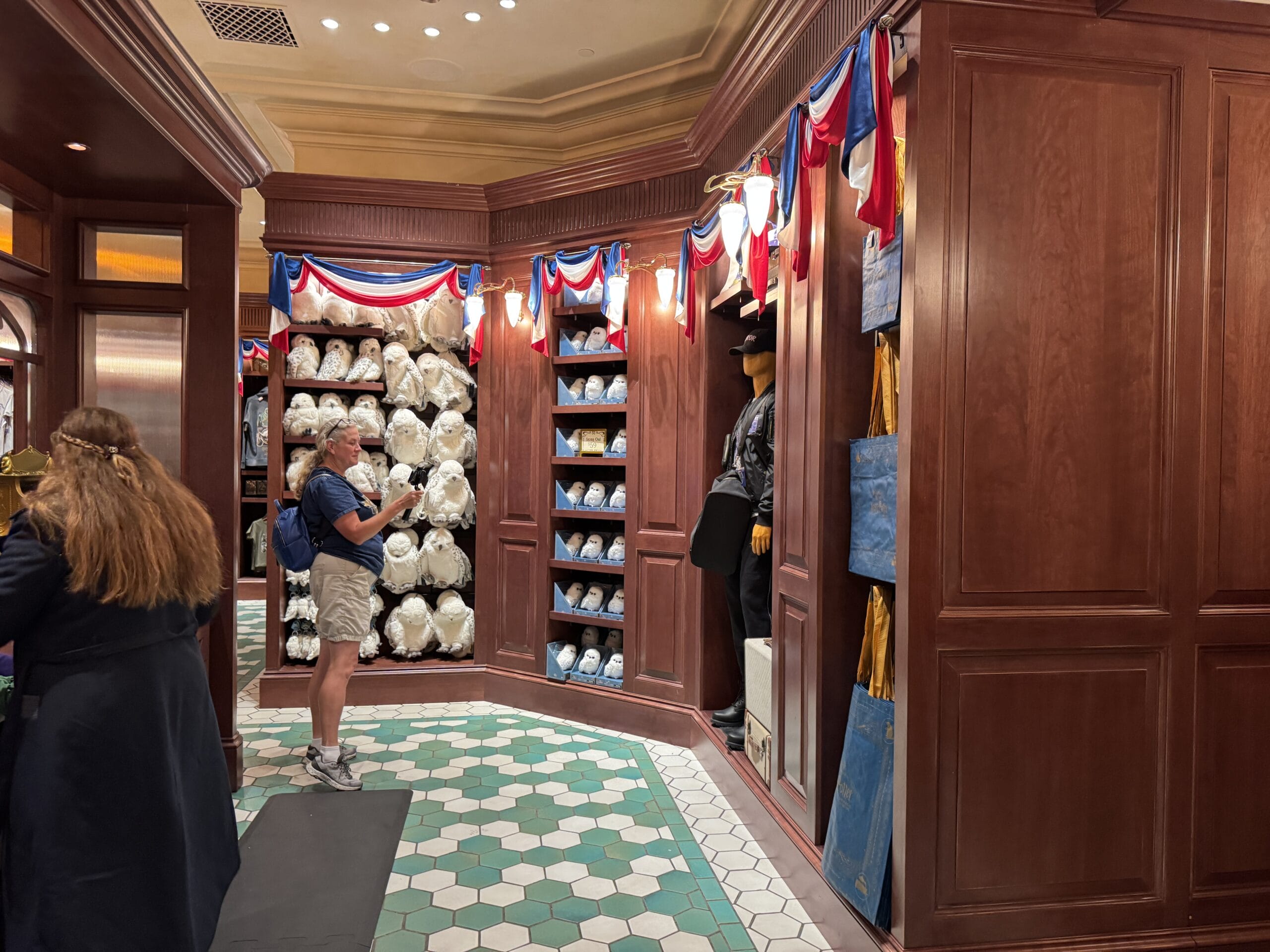 A man takes a photo in the Tour En Floo Shop, surrounded by plush toys and patriotic bunting at Epic Universe.