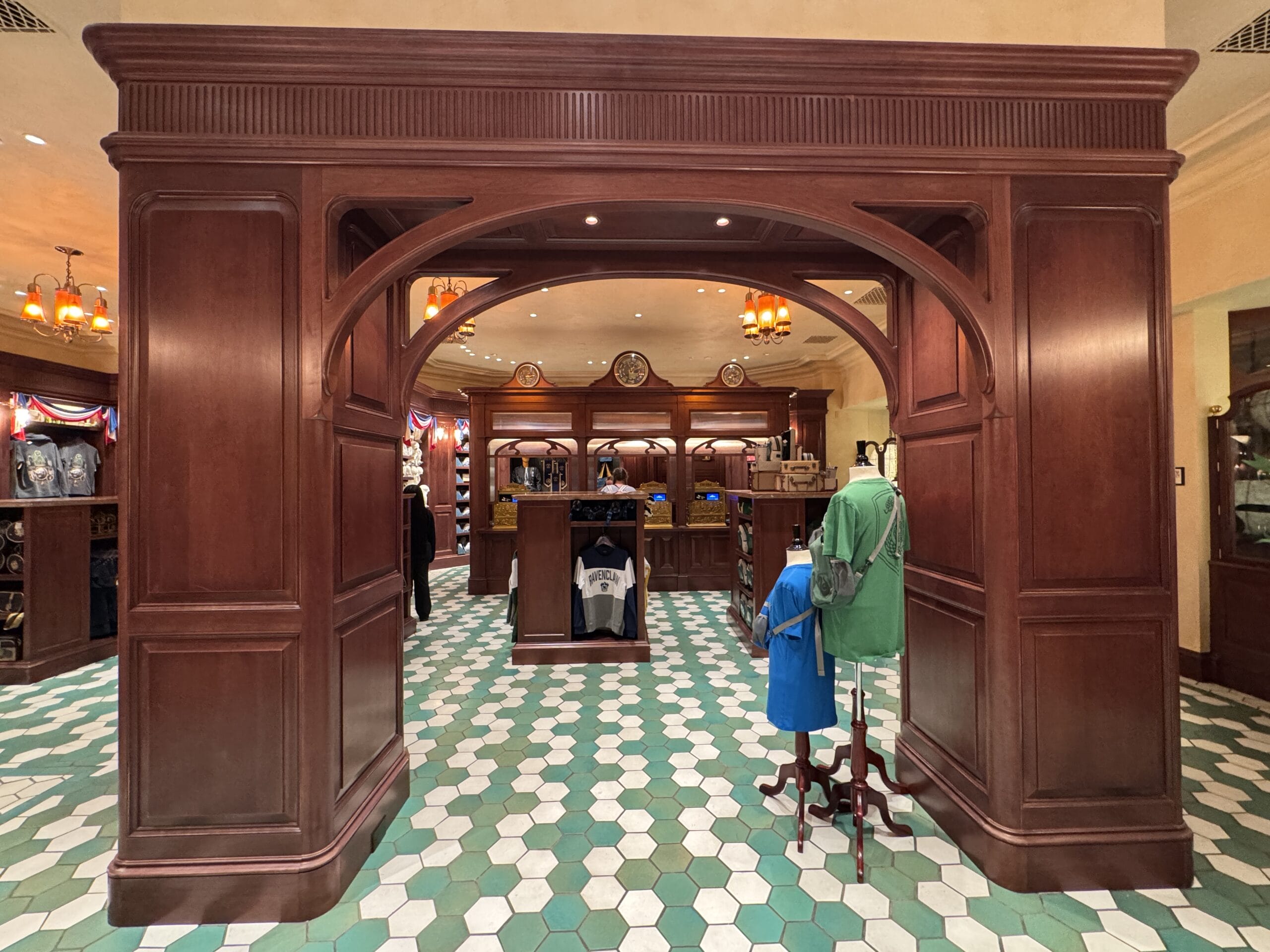 A wooden archway leads into the Tour En Floo Shop at Epic Universe, with clothing displays and hexagonal floor tiles.
