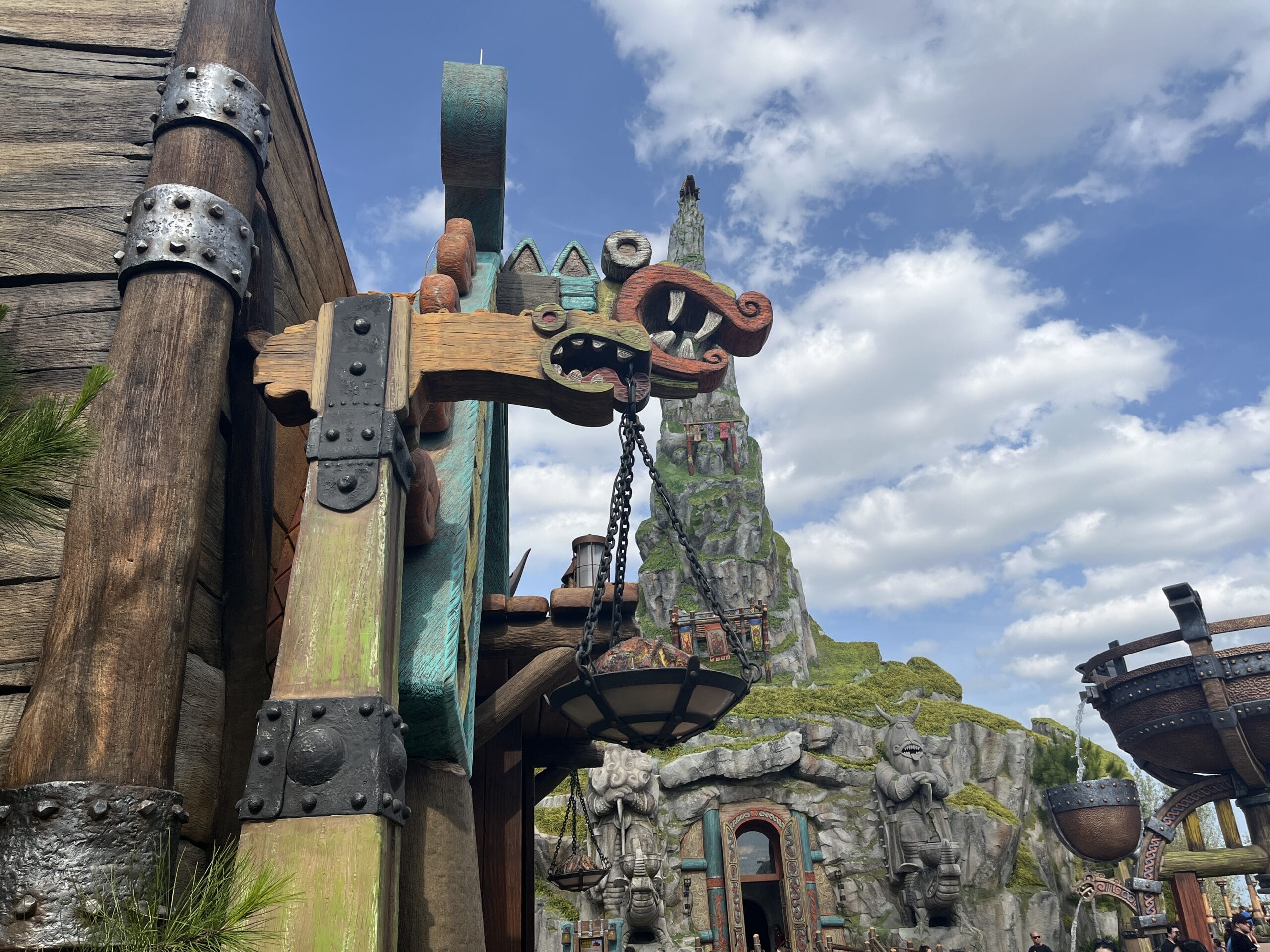 Wooden Norse dragon lantern near a fantasy mountain building under clear blue sky.
