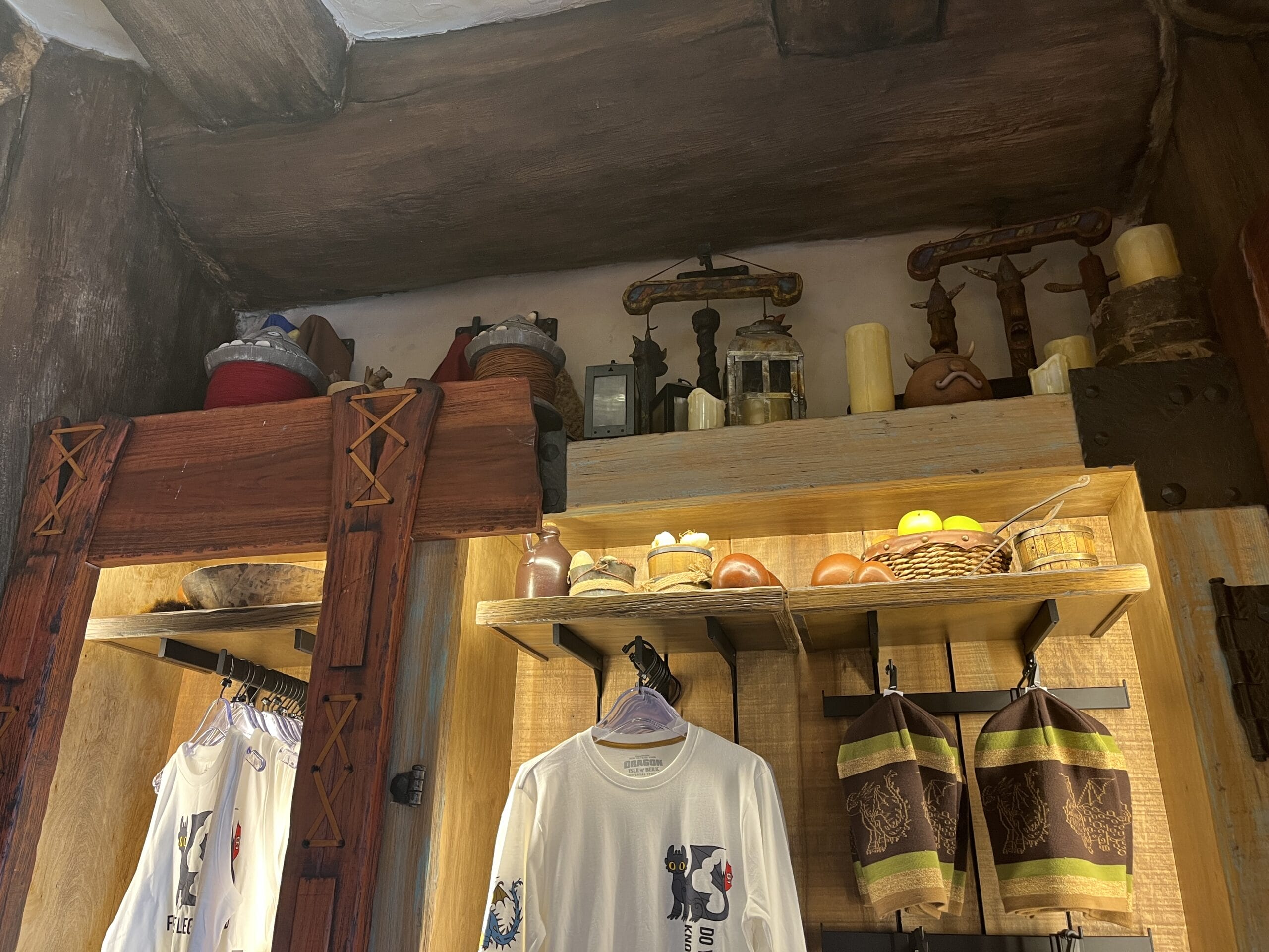 Shelves with candles, baskets, and Viking Traders decor above hanging shirts and towels in a rustic park shop.