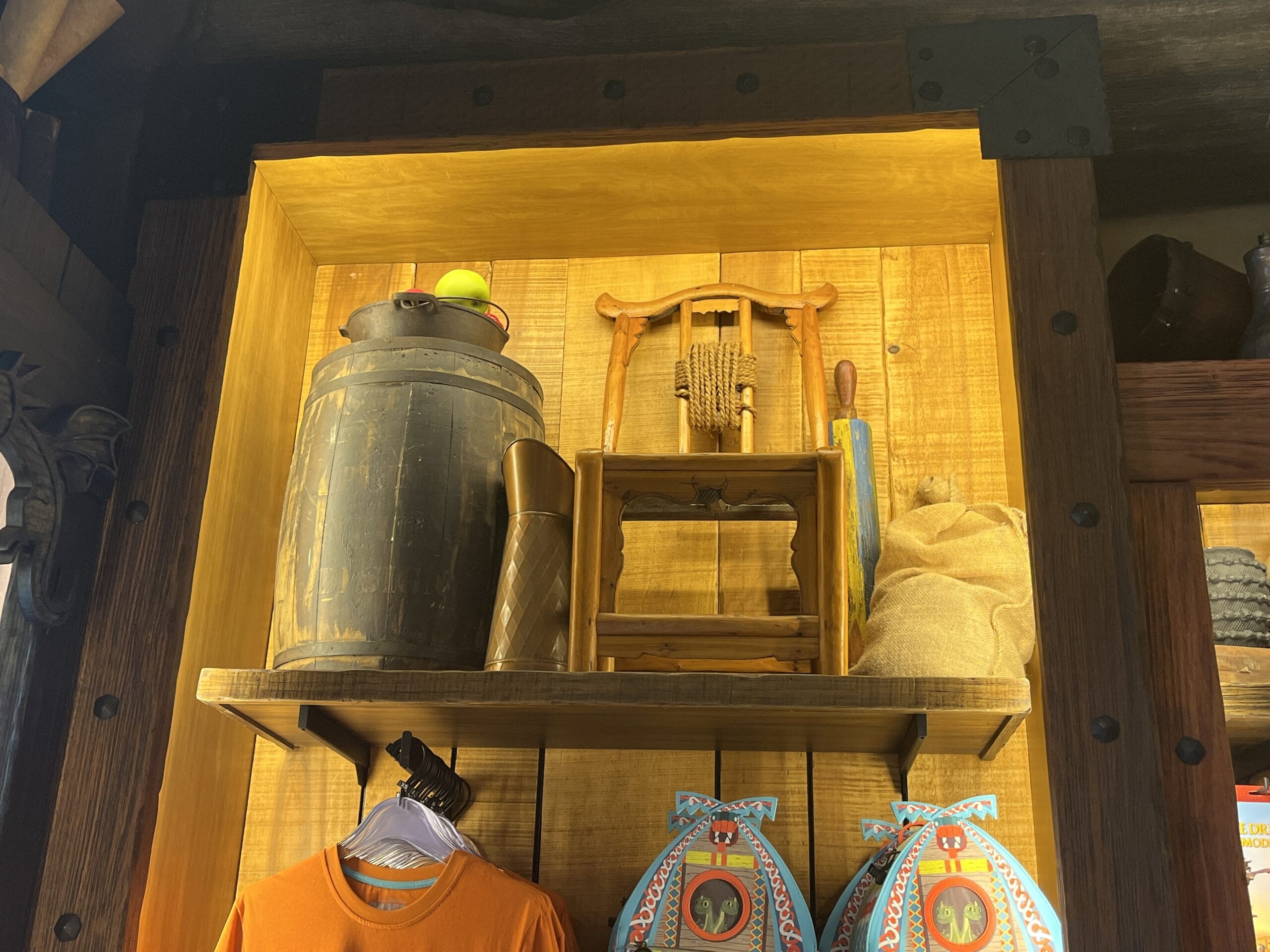 Wooden shelf at Epic Universe with Viking Traders barrel, butter churn, and games above orange shirts and toy souvenirs.