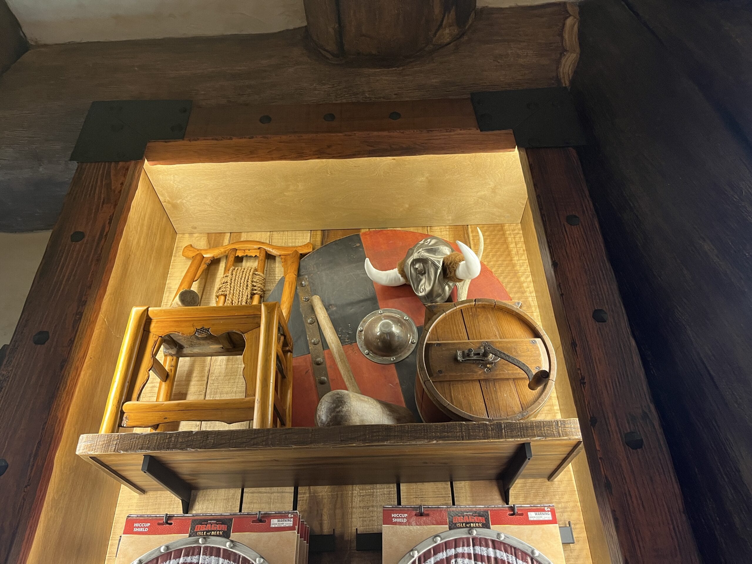 A display case featuring Viking Traders’ medieval weapons, shields, a helmet, and a stool.