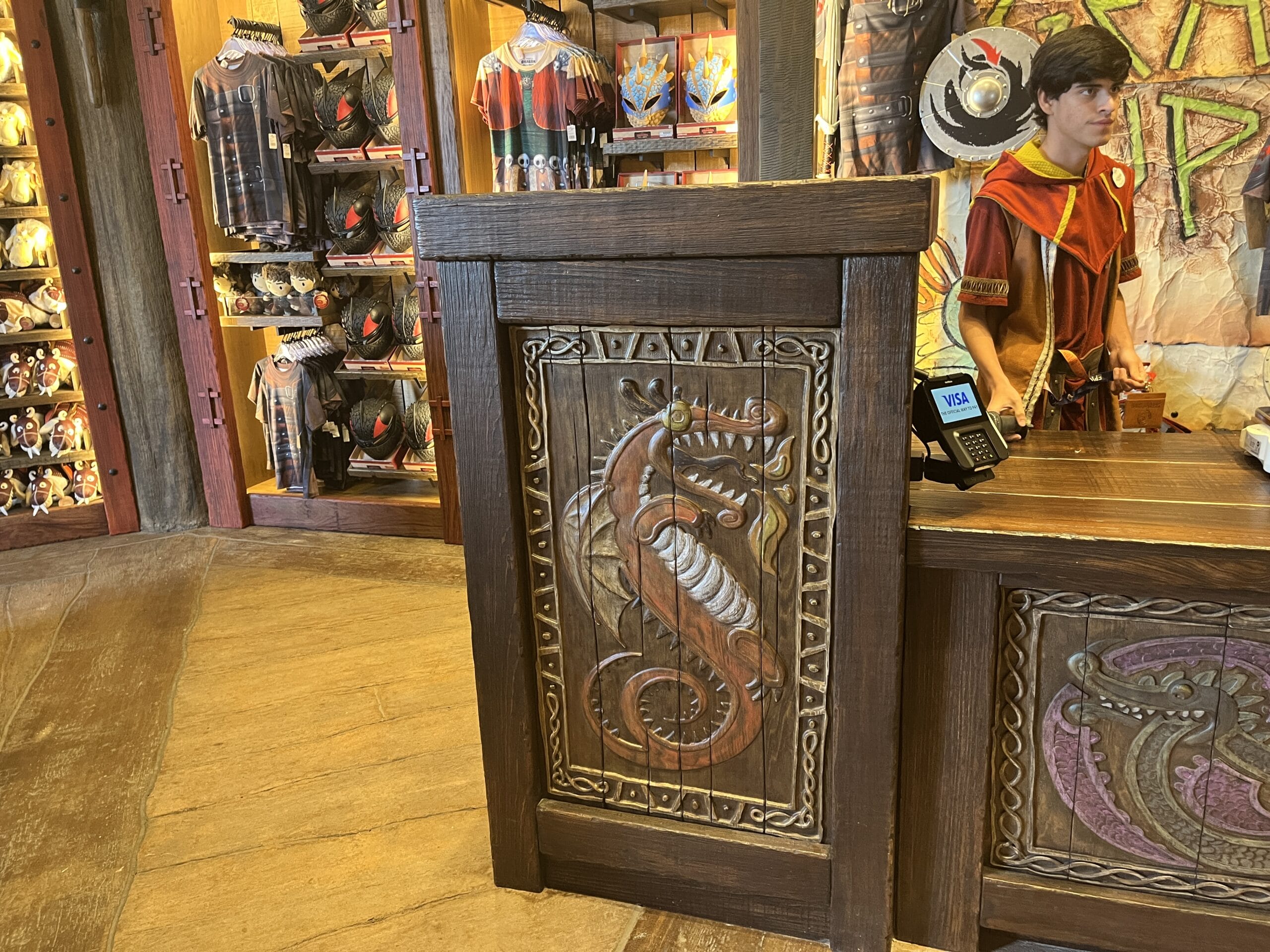 Wooden counter with carved dragon at Viking Traders gift shop, surrounded by Norse-themed merchandise and staff in costume.