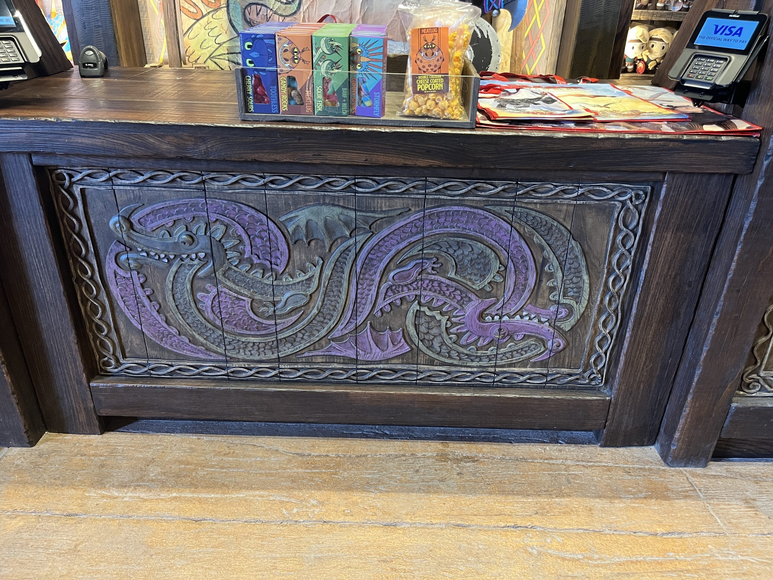Carved wooden counter with Viking Traders’ purple and green dragon, next to registers and souvenirs.