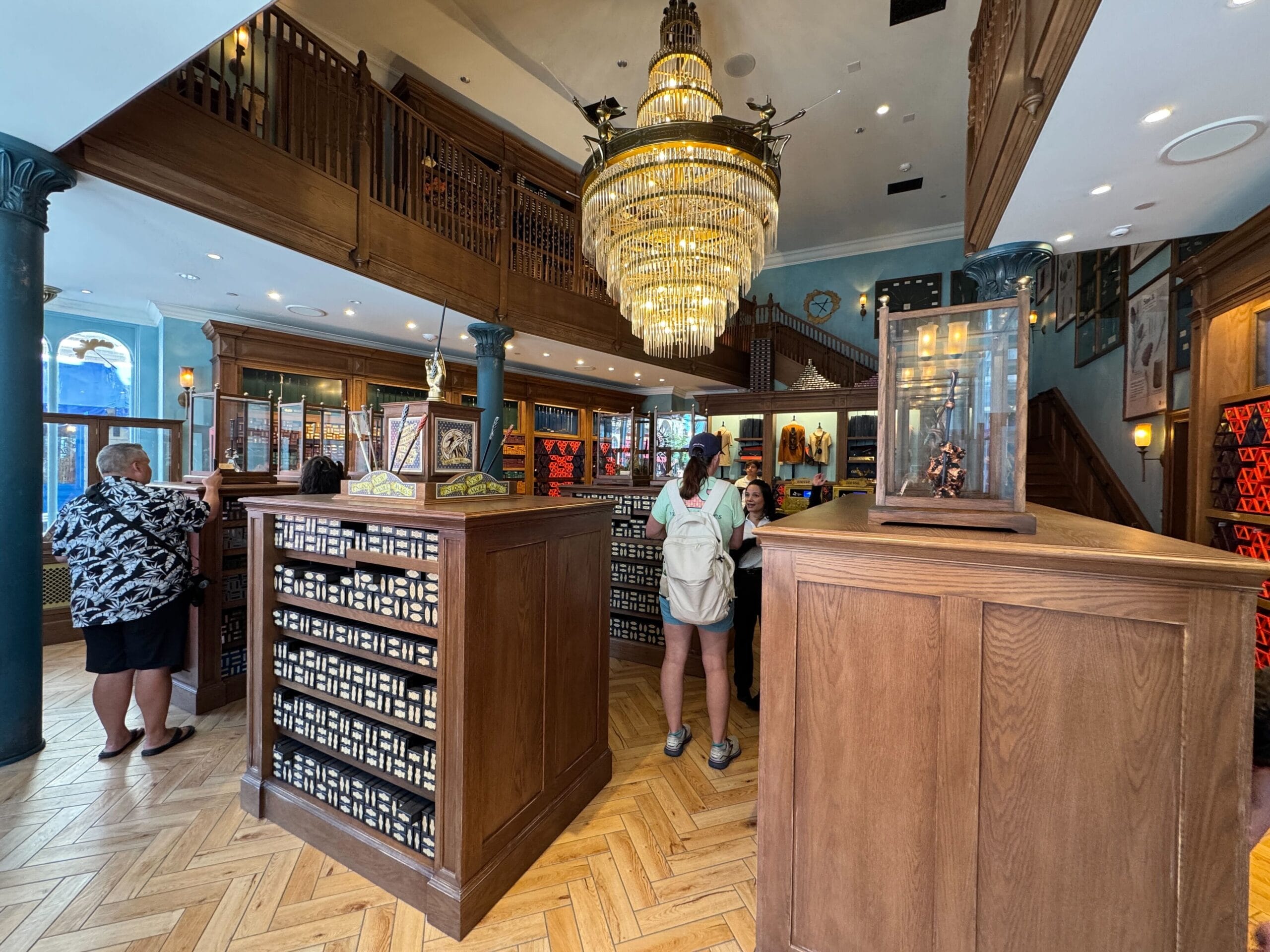 People browsing and shopping inside a well-lit Cosme Acajor store with wooden shelves, a large chandelier, and framed pictures on the walls.