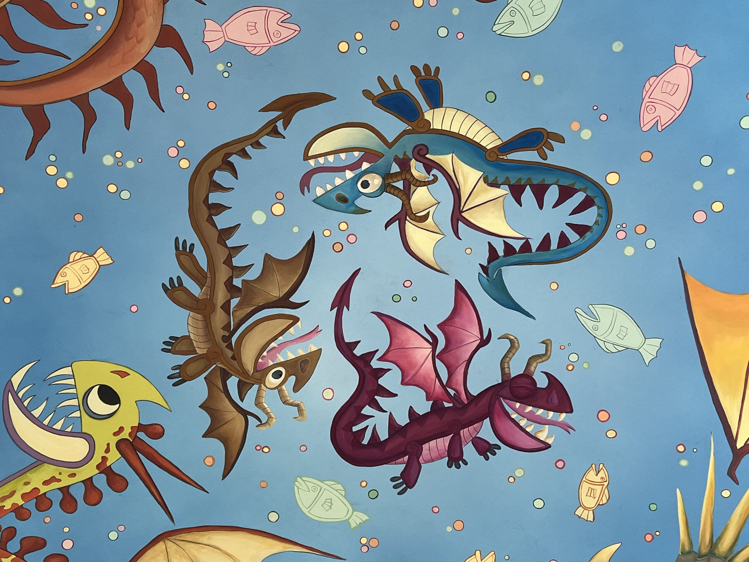 Three colorful cartoon dragons from How to Treat Your Dragon swim among fish on a blue background with bubbles.