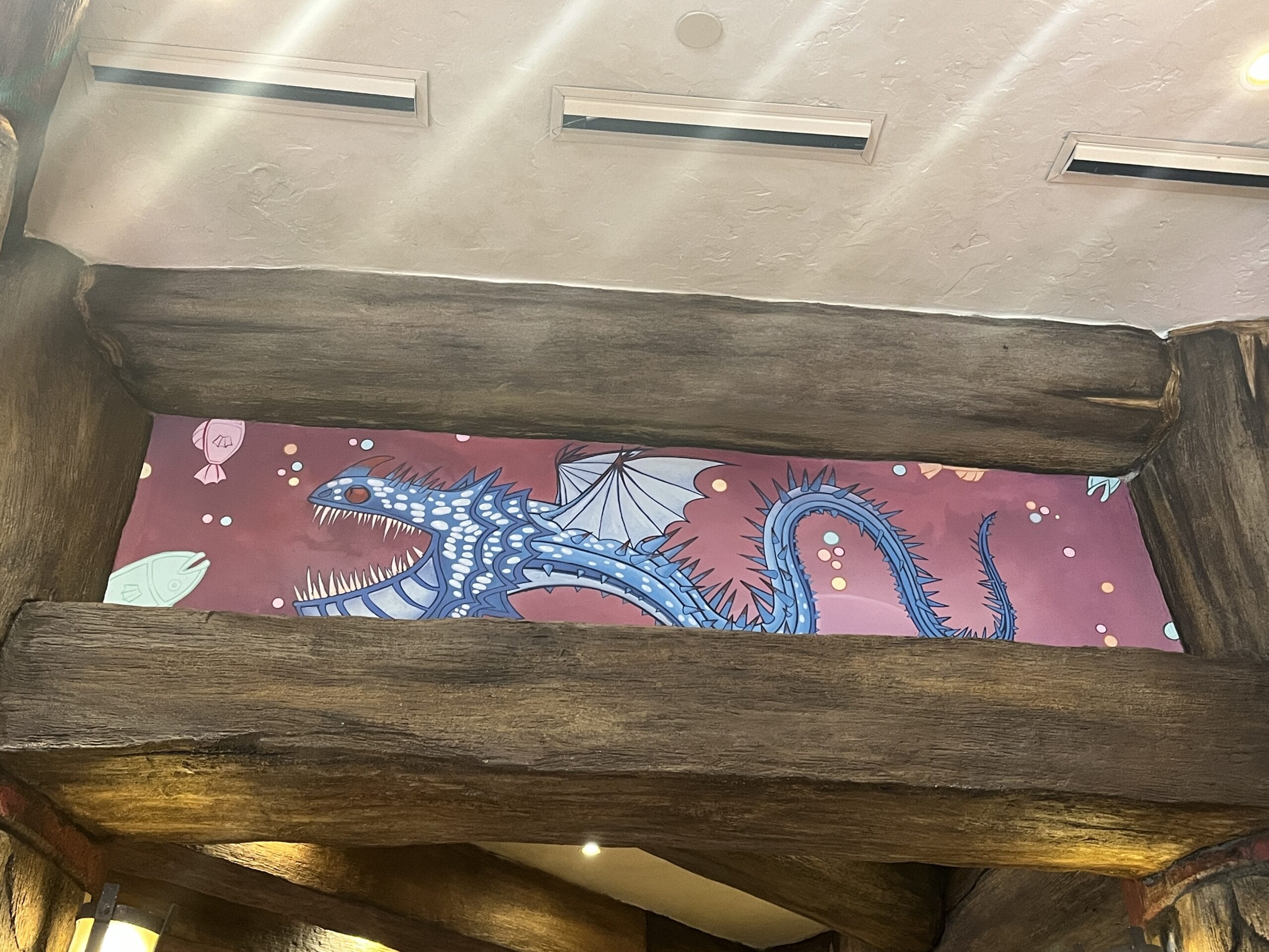 Colorful mural of a blue dragon with white wings, inspired by How to Treat Your Dragon, on a red background.