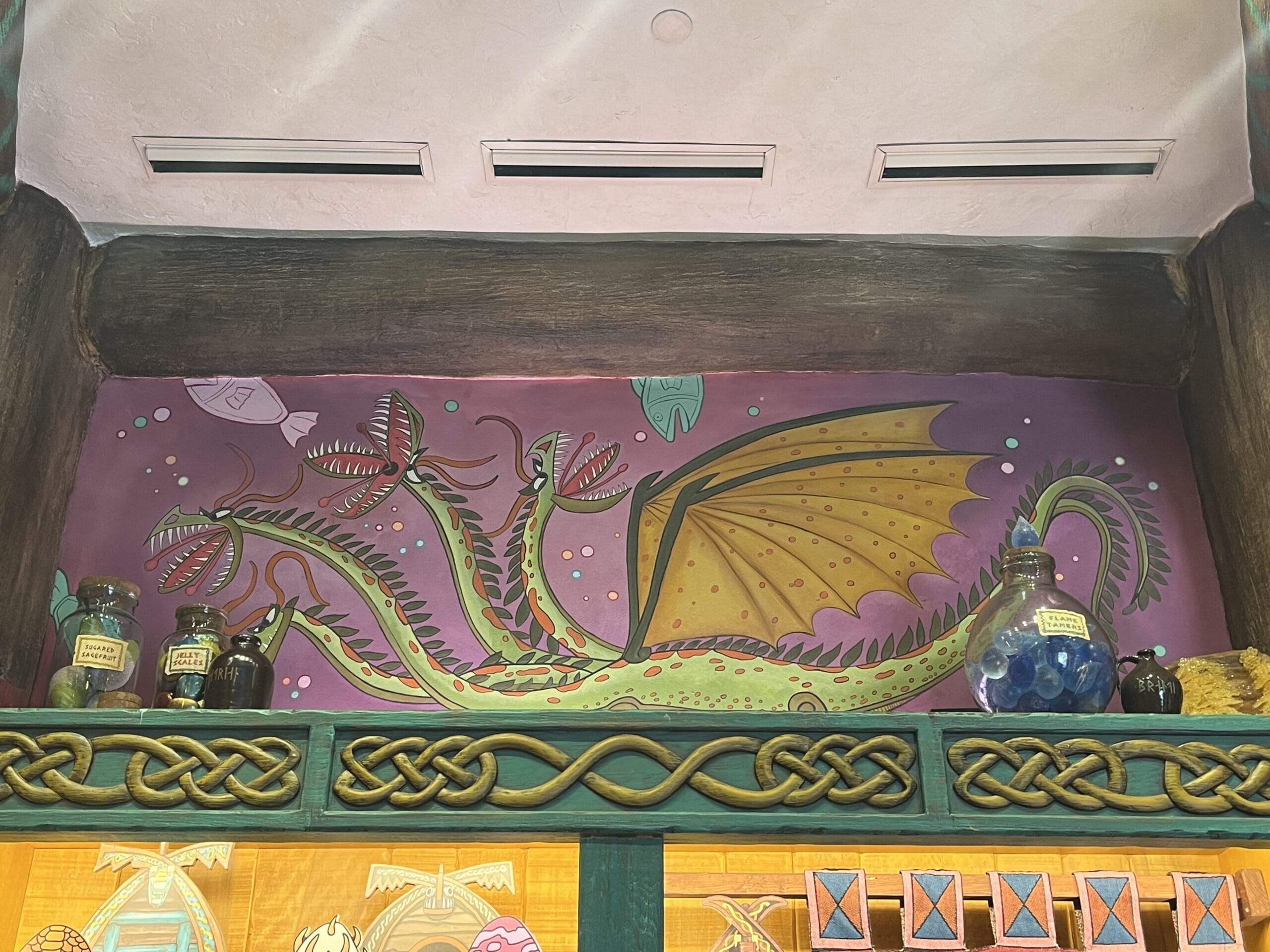Colorful mural of a multi-headed dragon above jars, framed by Celtic knotwork—perfect for How to Treat Your Dragon fans.