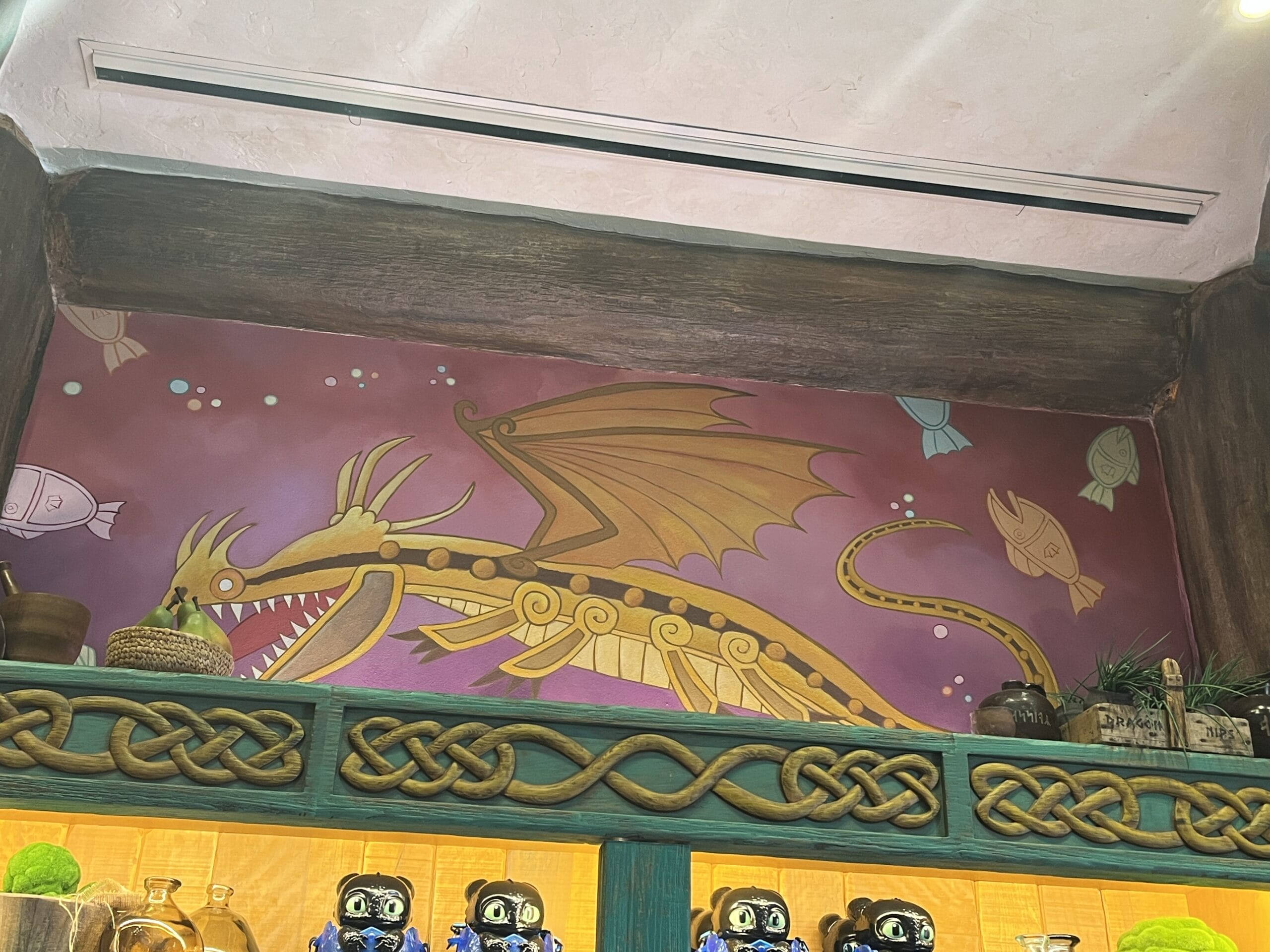 A mural of a stylized yellow dragon with wings, inspired by How to Treat Your Dragon, above a shelf with plants and jars.