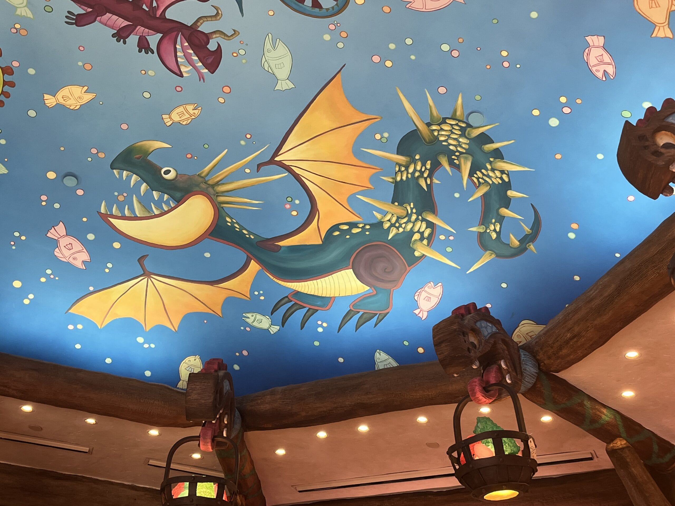 Colorful ceiling mural inspired by How to Treat Your Dragon, with a yellow-winged cartoon dragon and whimsical fish on blue.