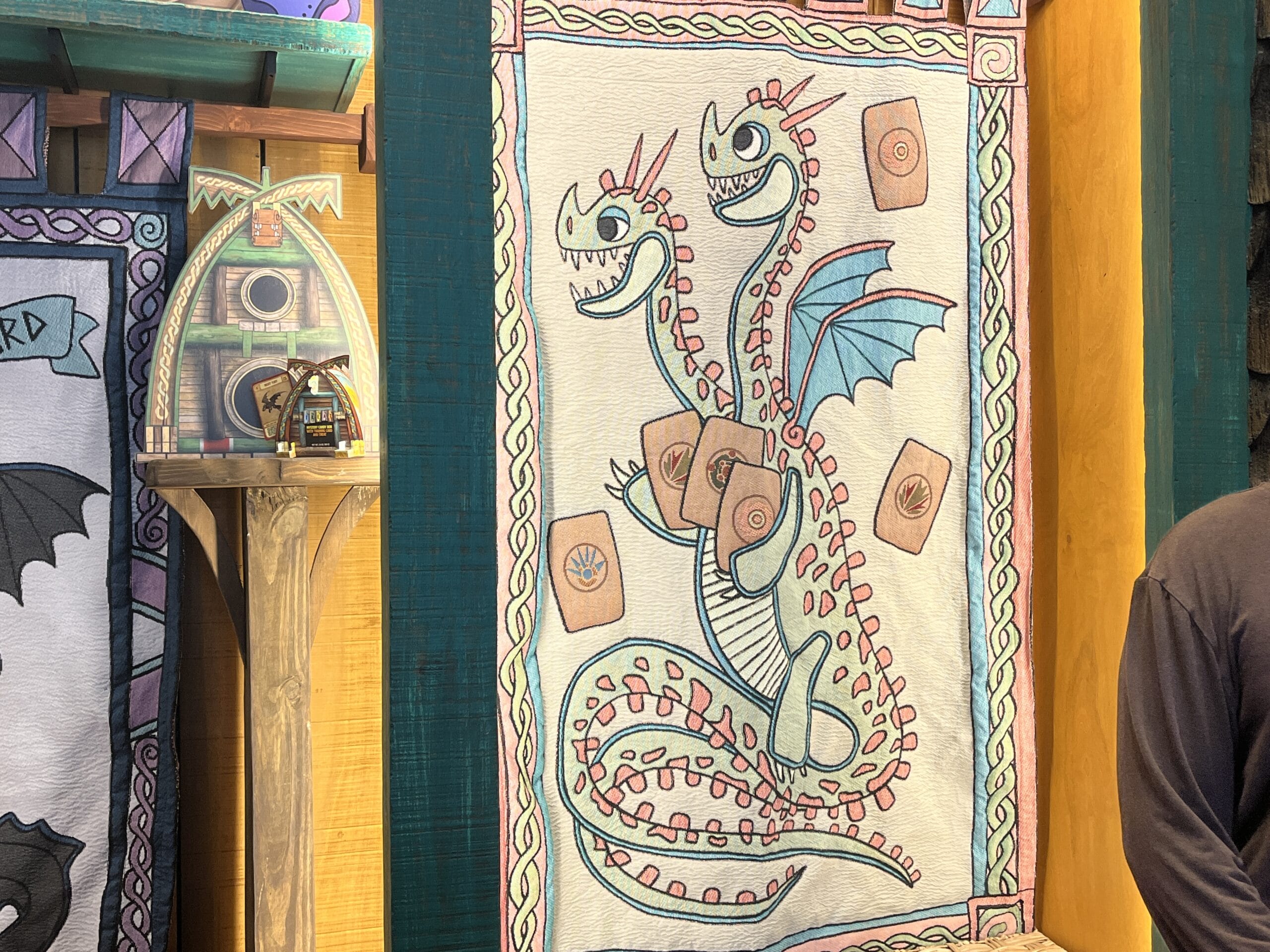 Colorful How to Treat Your Dragon tapestry of a two-headed, winged dragon with red spikes on a yellow and green wall.