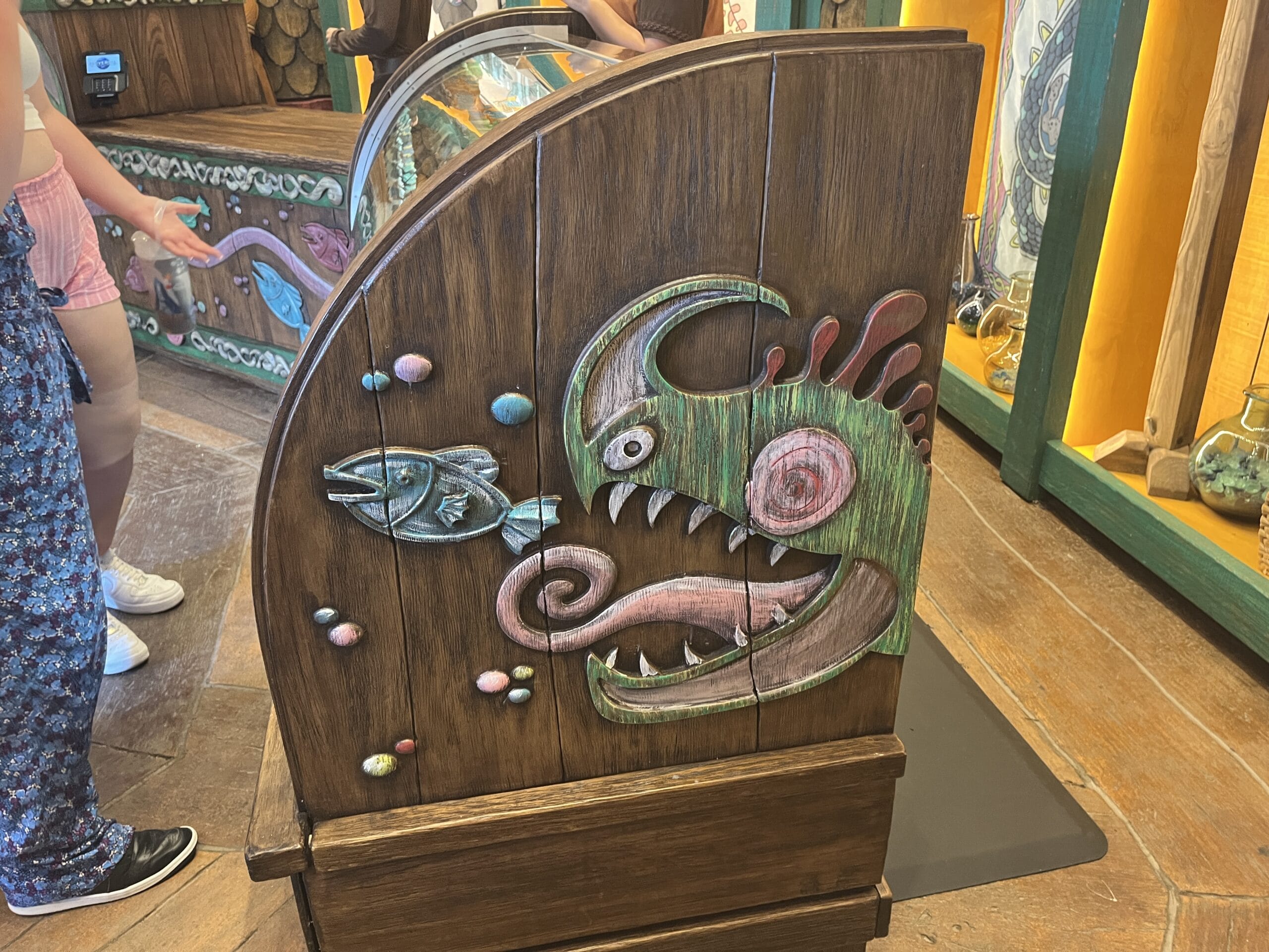 Wooden counter with a colorful How to Treat Your Dragon-style sea monster eating a fish, inside an ocean-themed store.