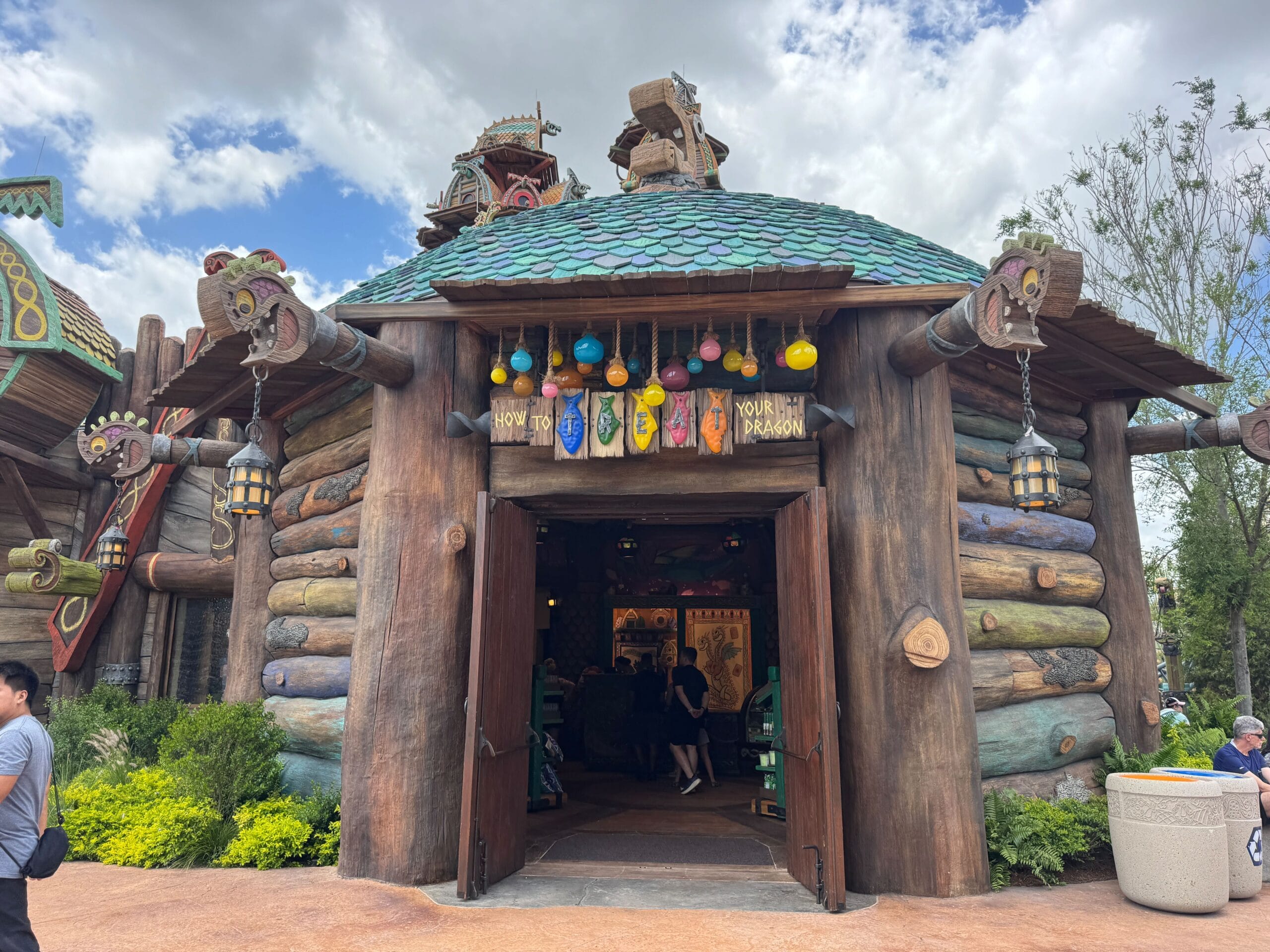 A round, wooden How to Treat Your Dragon shop with a dragon sign and colorful lanterns at Epic Universe.