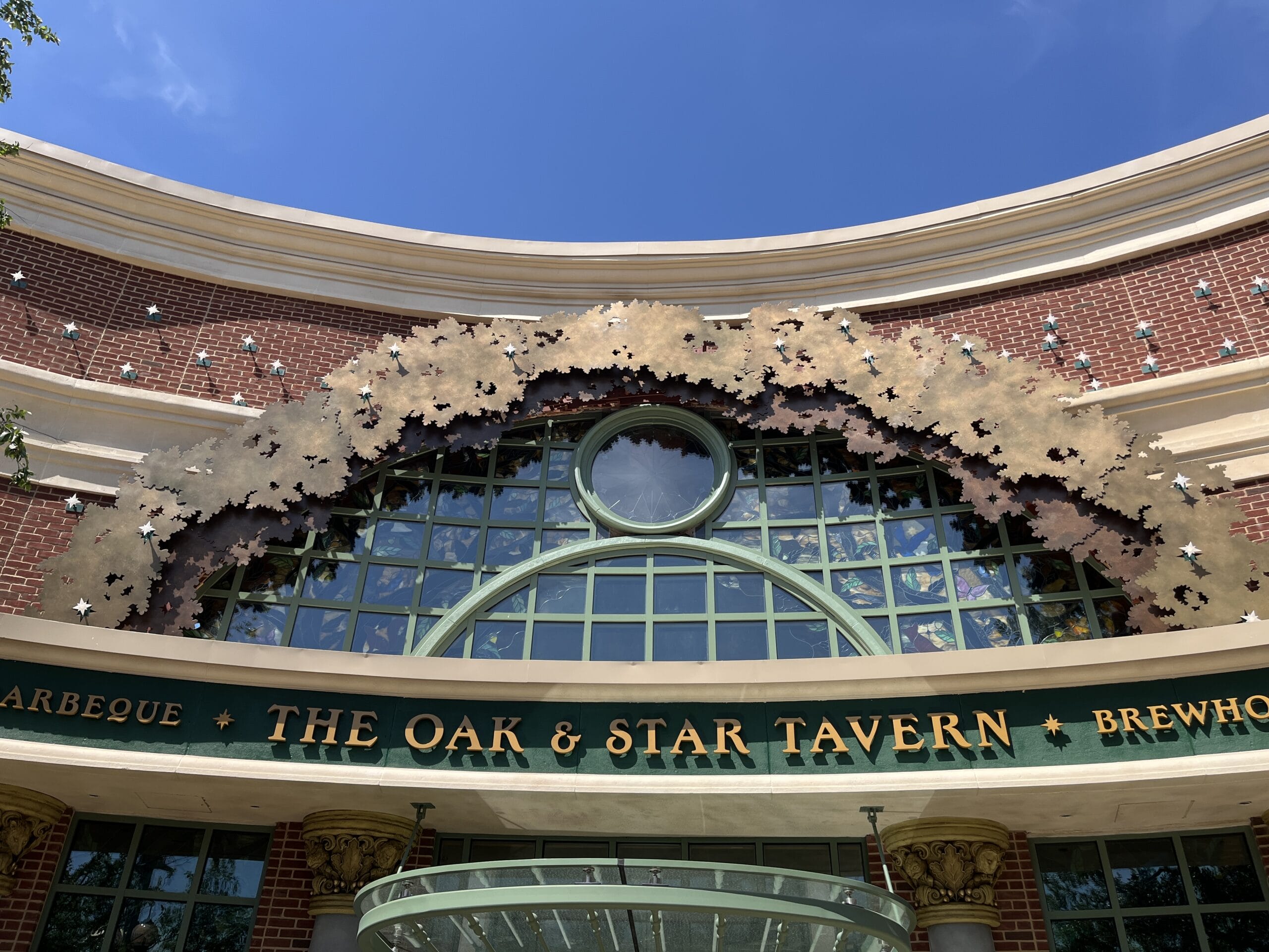 The Oak & Star Tavern entrance boasts gold leaf above green windows, shining beneath a clear blue sky.