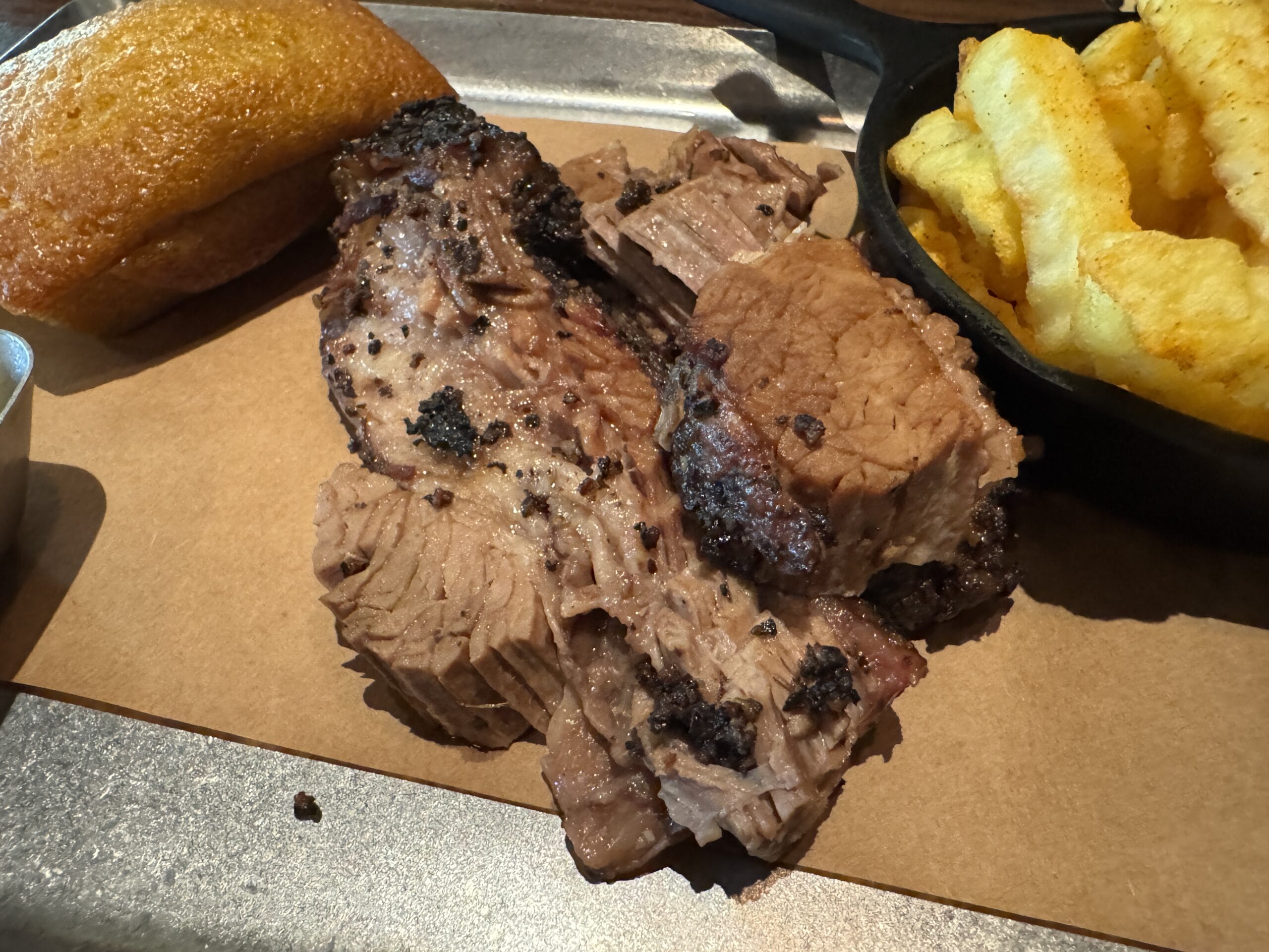 Slices of smoked brisket with crinkle-cut fries and cornbread, plated at The Oak & Star Tavern—reminiscent of Disney park fare.