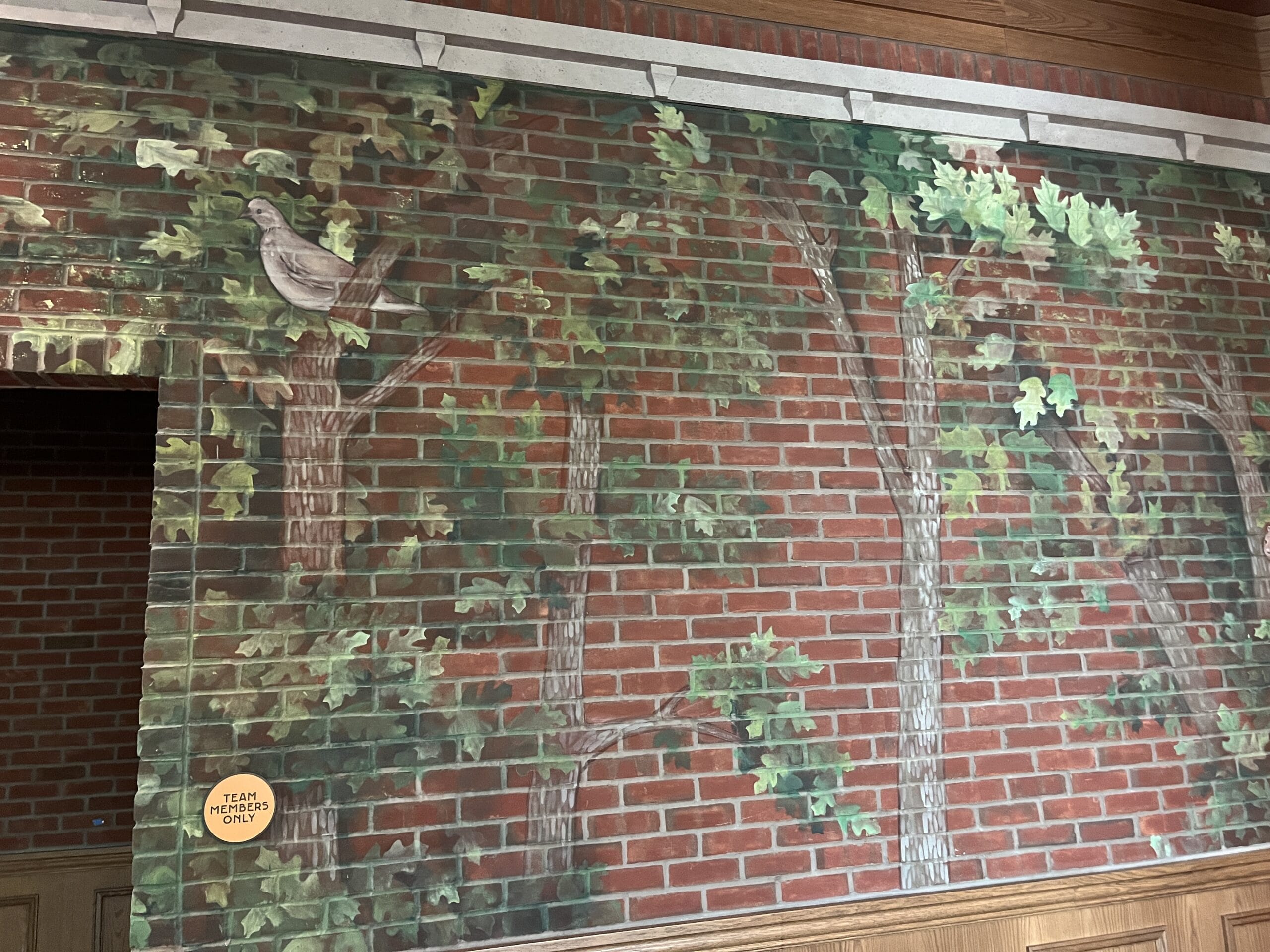 Mural of trees and a bird on a brick wall at The Oak & Star Tavern, with a "TEAM MEMBERS ONLY" sign—no Disney castle present.