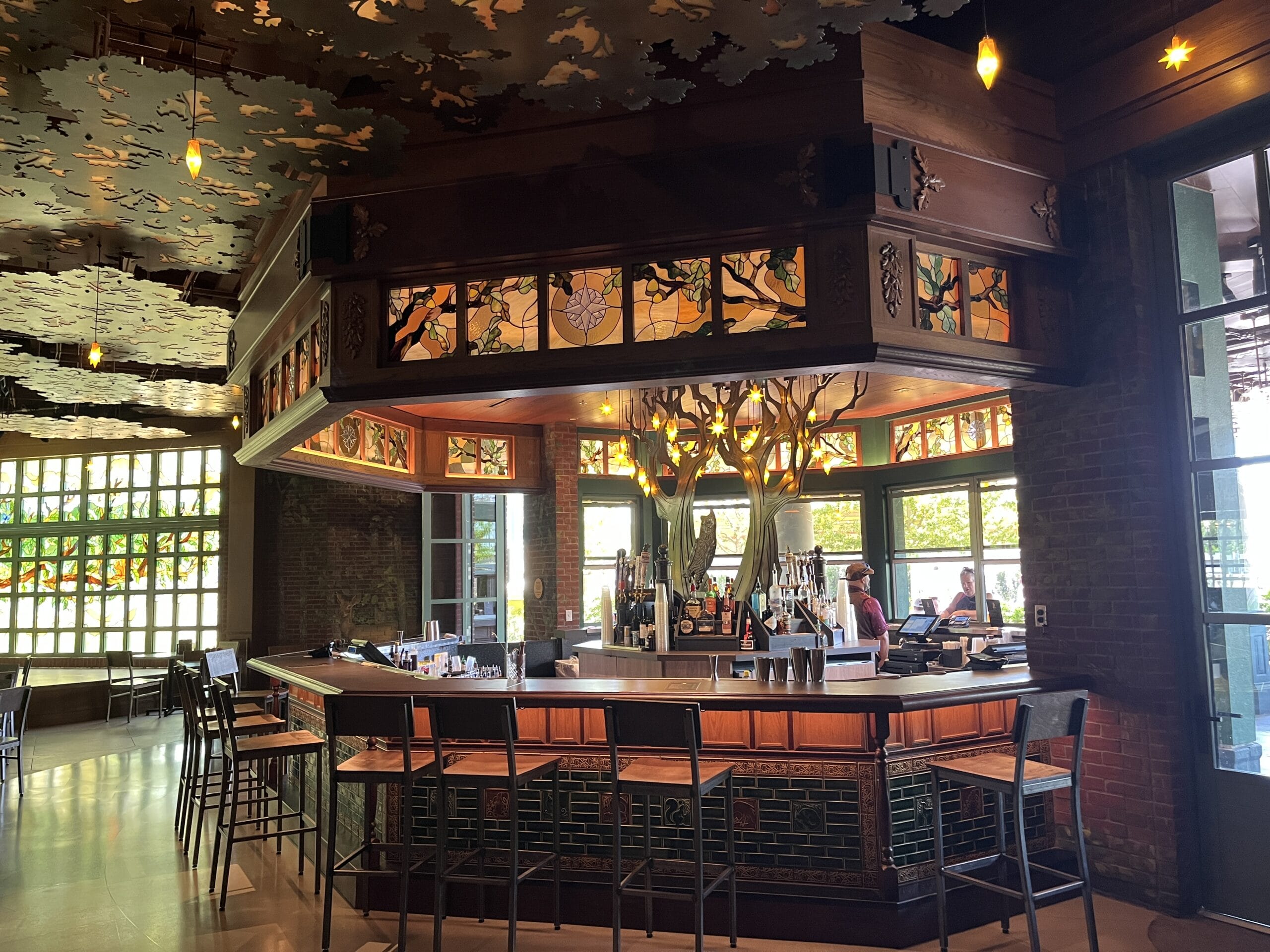 The Oak & Star Tavern is a stylish bar with stained glass, wooden decor, and whimsical antler lights, evoking Disney park charm.