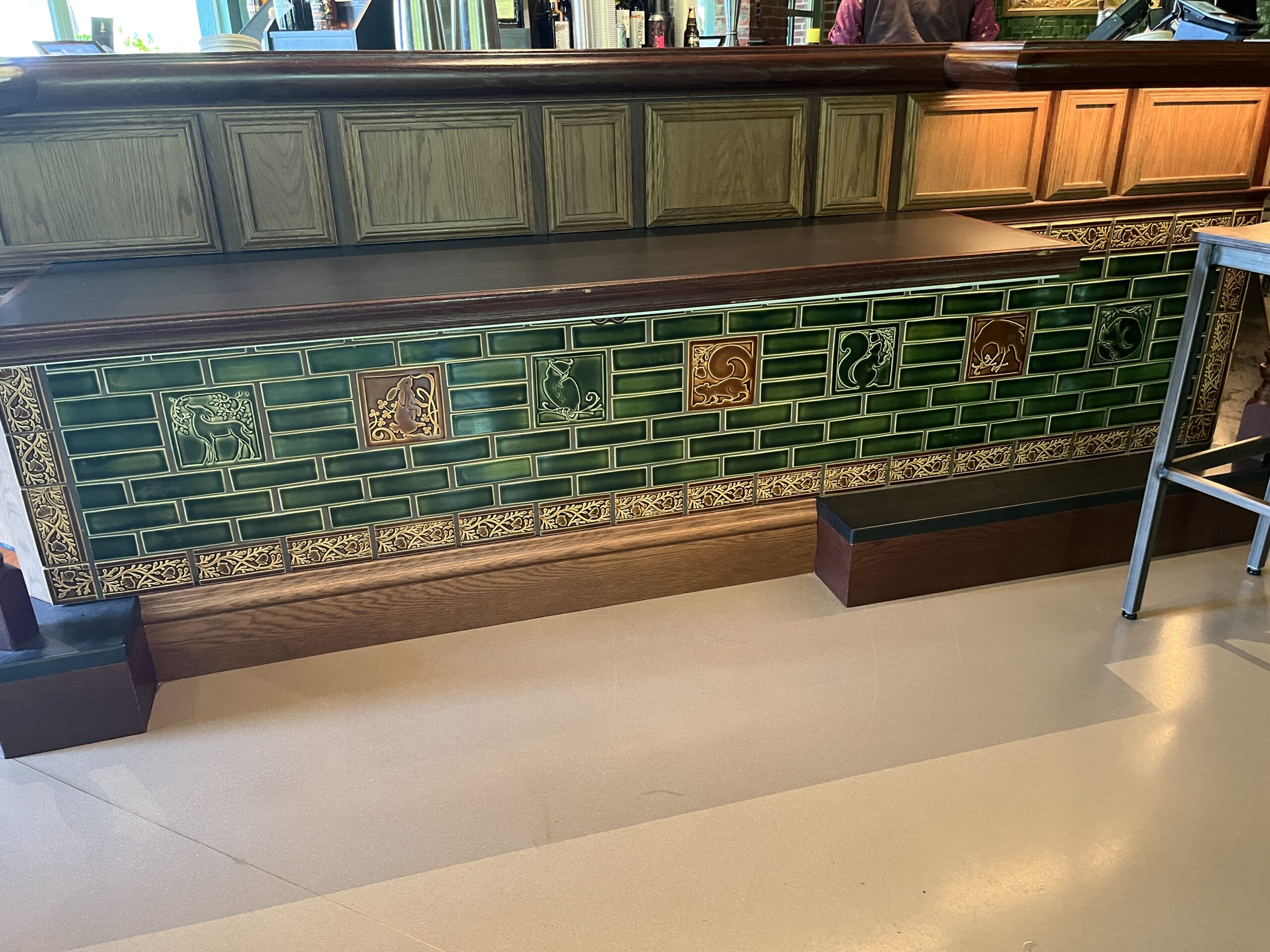 The Oak & Star Tavern bar front features green animal tiles and wood accents, evoking the whimsy found in Disney park details.