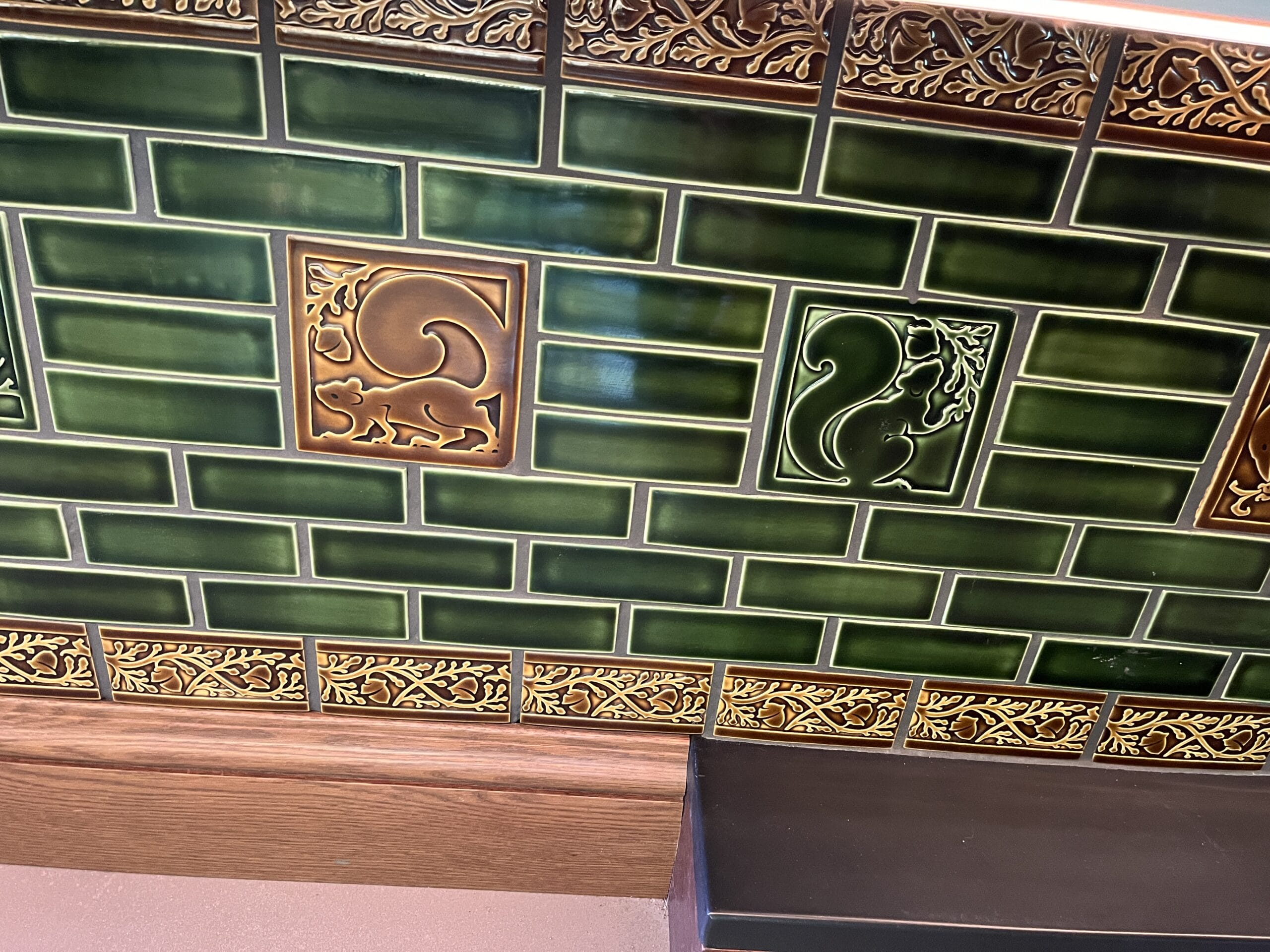 Ornate green tiles with embossed squirrels and leafy patterns, wood-trimmed, reminiscent of whimsical Disney Park tavern decor.