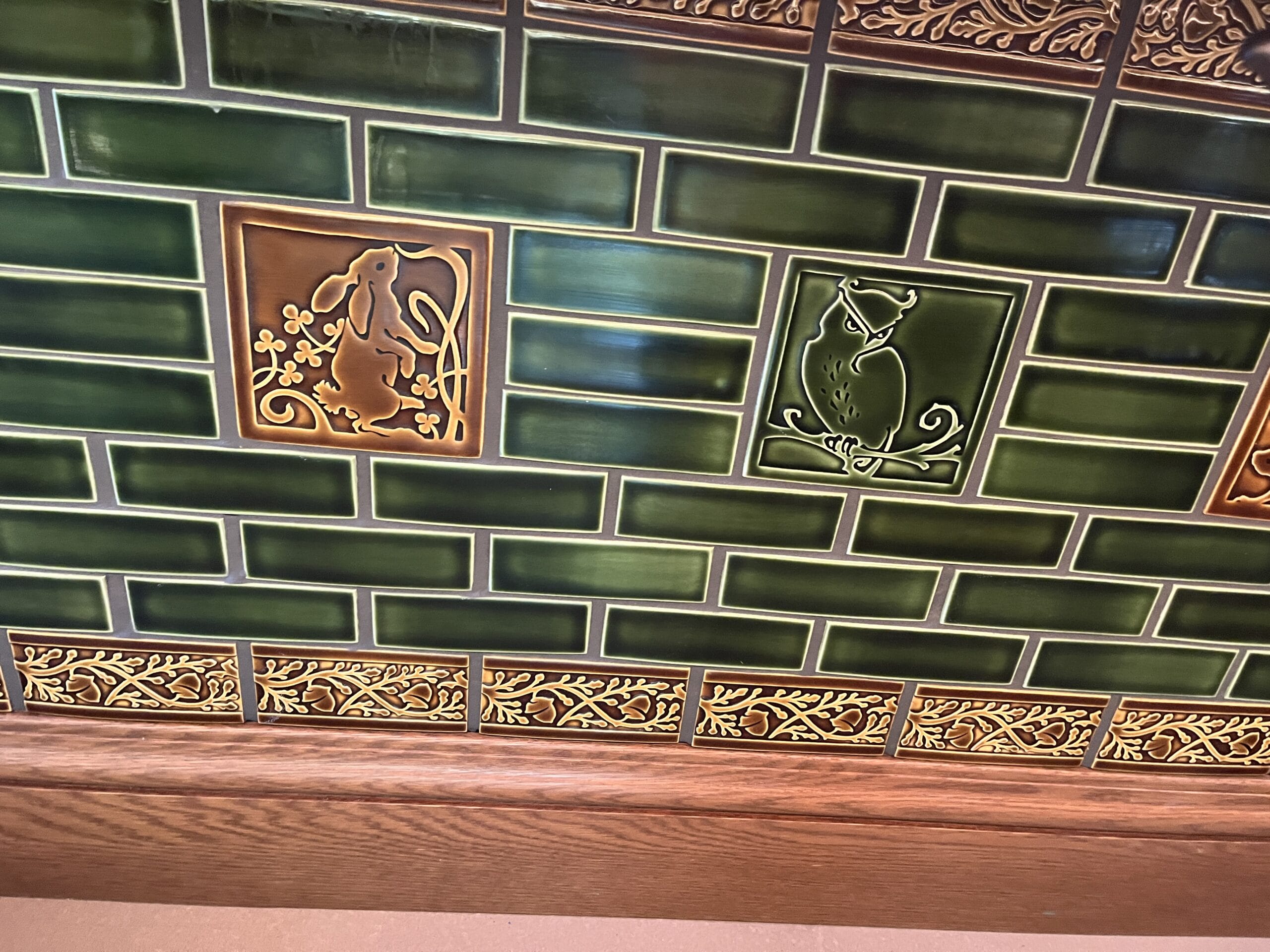 Green tiled wall at The Oak & Star Tavern, featuring whimsical animal tiles like a rabbit and owl, reminiscent of Fantasyland decor.