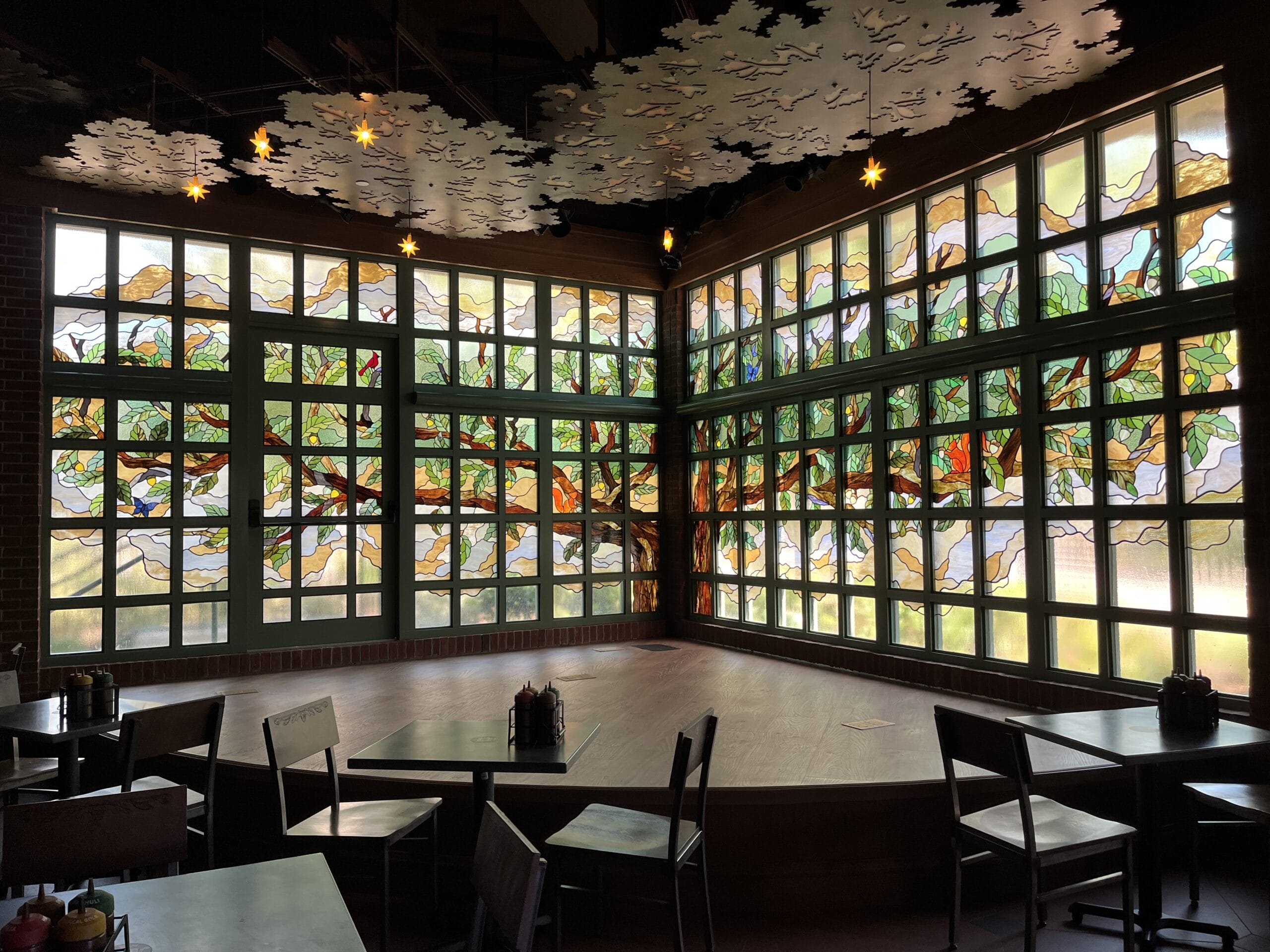 A cozy tavern stage with stained glass windows, empty tables and chairs—evoking Disney Park lounges, but no castle in view.