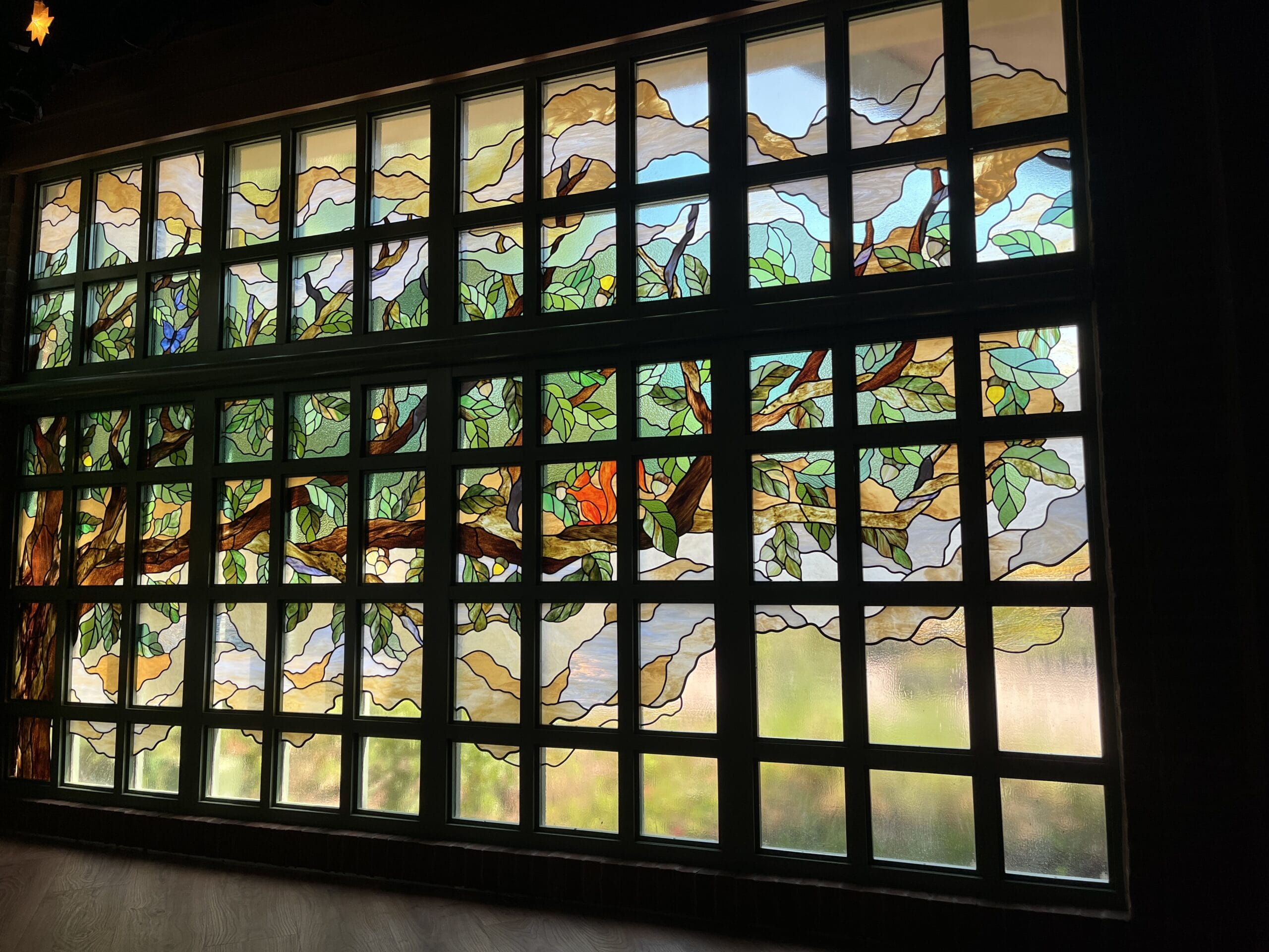 Stained glass window at The Oak & Star Tavern, showing a vibrant tree—rich greens, browns, and blues—reminiscent of Disney park detail.