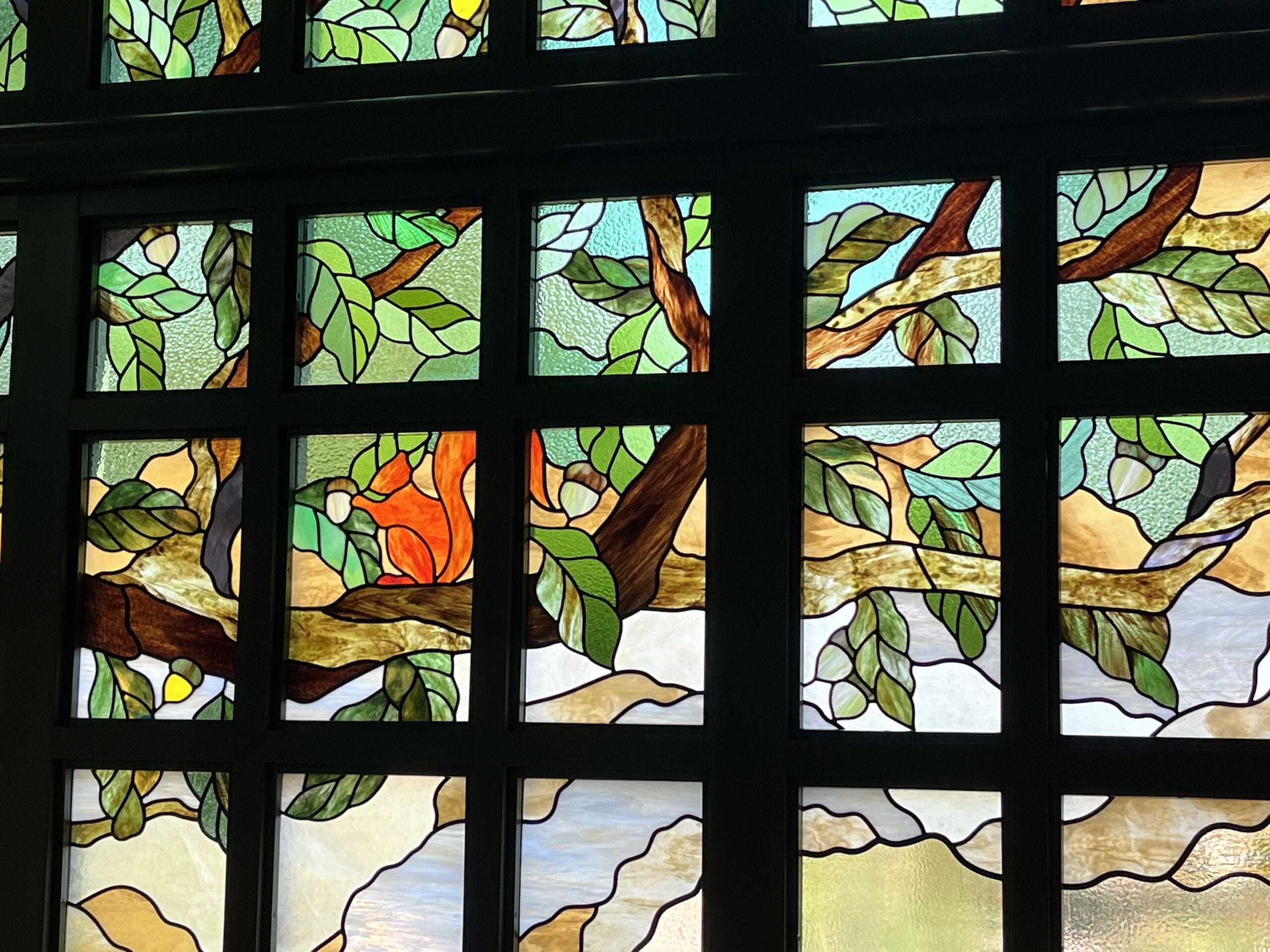 Stained glass window at The Oak & Star Tavern, colorful tree branch, green leaves, orange fruit—no Disney castle elements visible.
