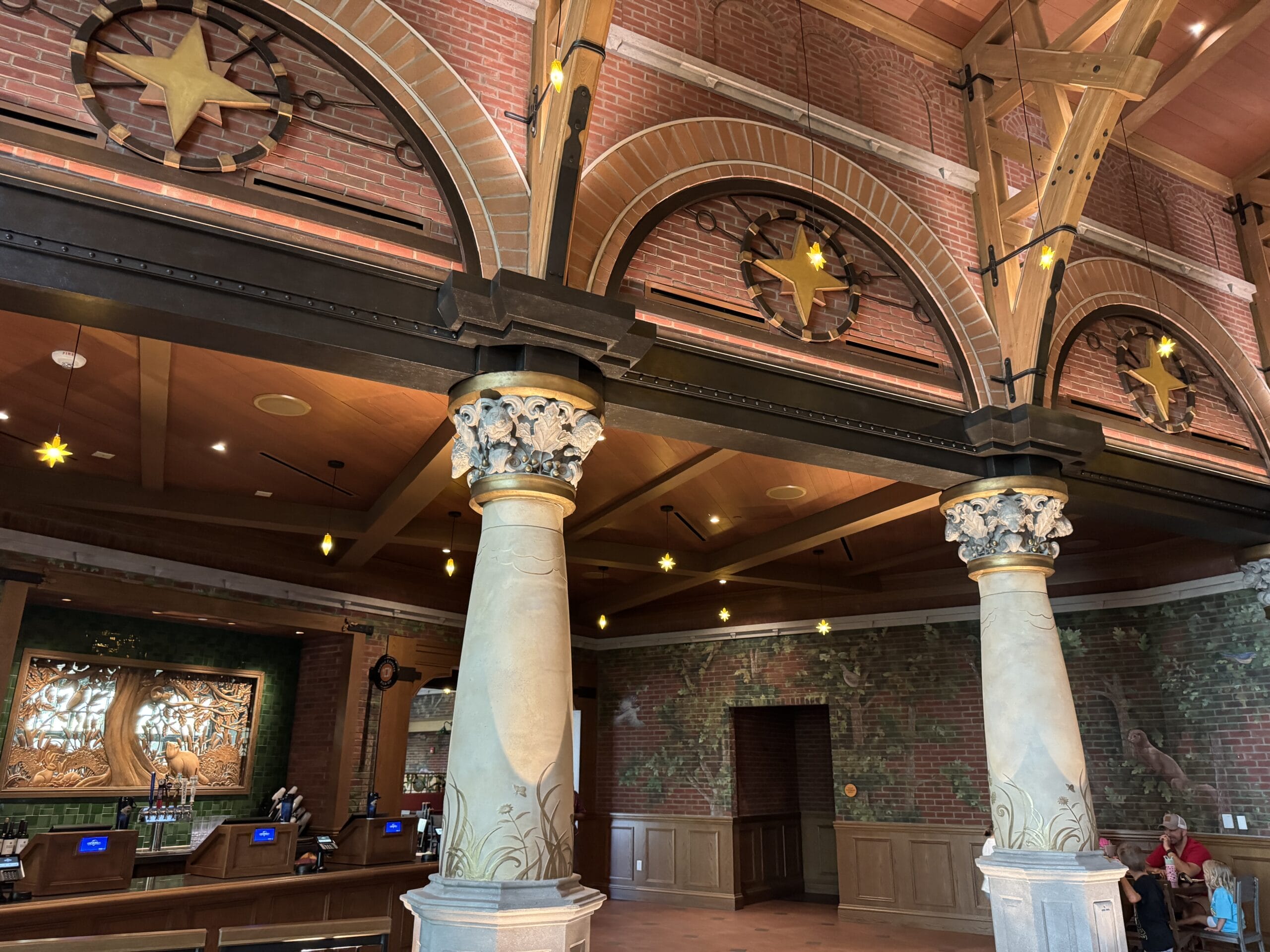 Lobby of The Oak & Star Tavern, with Disney-esque ornate columns, brick walls, arched windows, star decor, and a left-side counter.