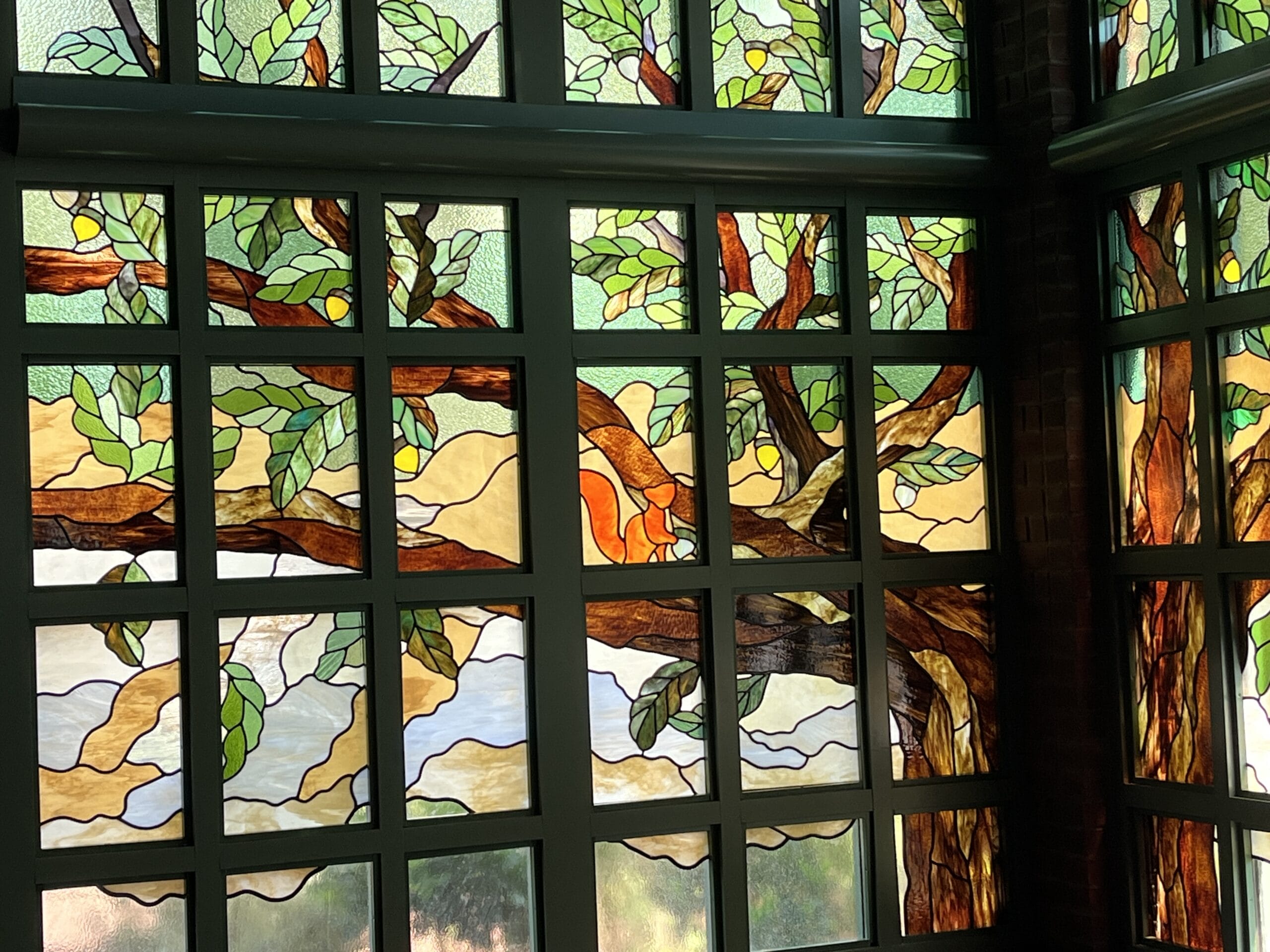 Stained glass at The Oak & Star Tavern features a tree with green leaves, yellow fruit, and a bright sky—distinct from any Disney castle.