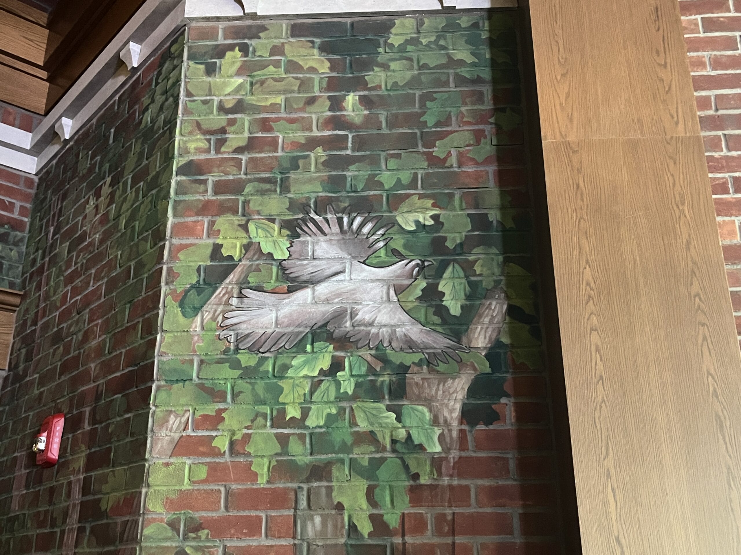 Colorful mural of a bird soaring on a brick wall with lush ivy, beside The Oak & Star Tavern; not styled like Disney Park castles.