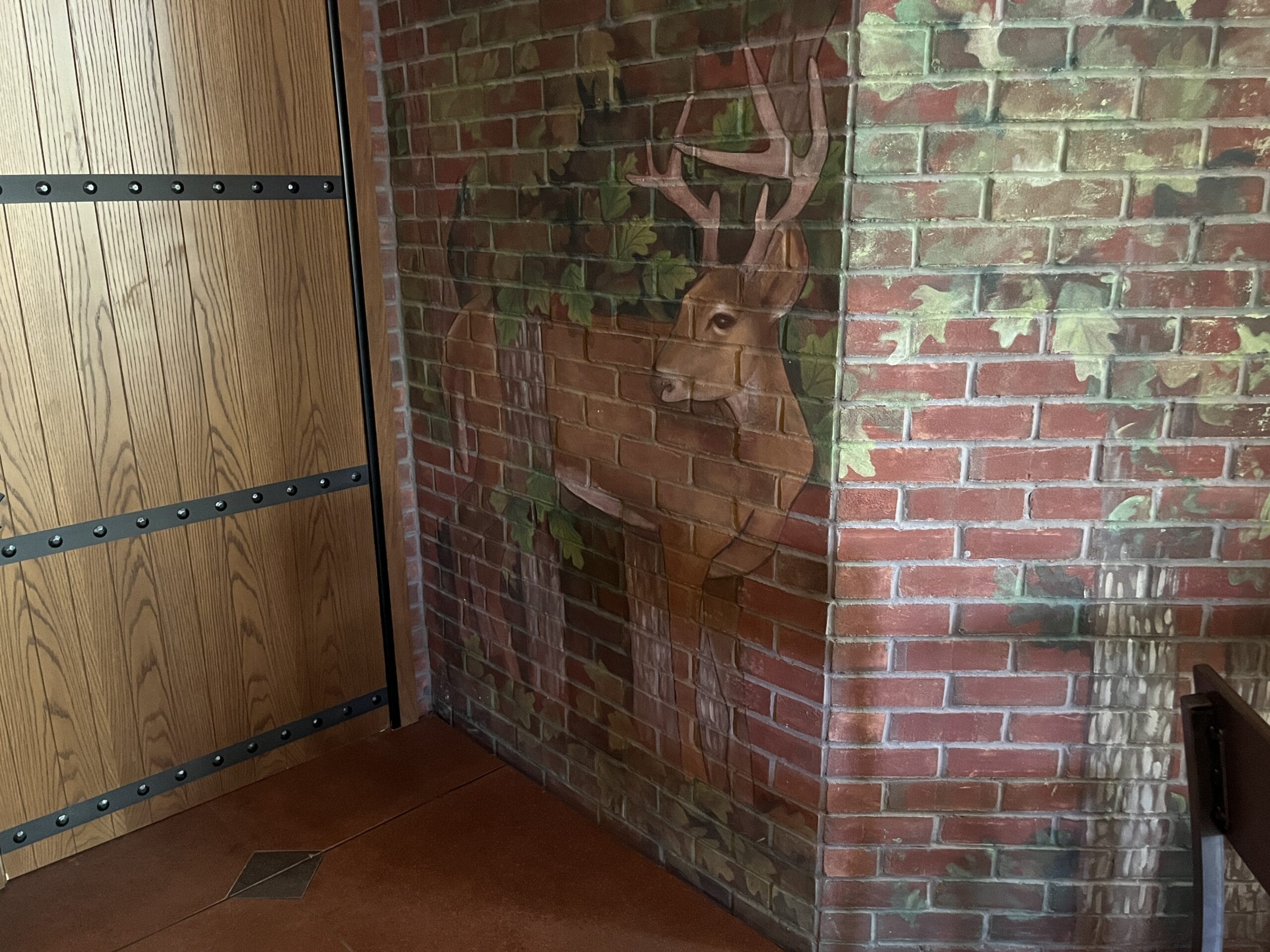 A mural of a deer blends into a brick wall near The Oak & Star Tavern, with Disney-style painted leaves and tree trunks by the door.