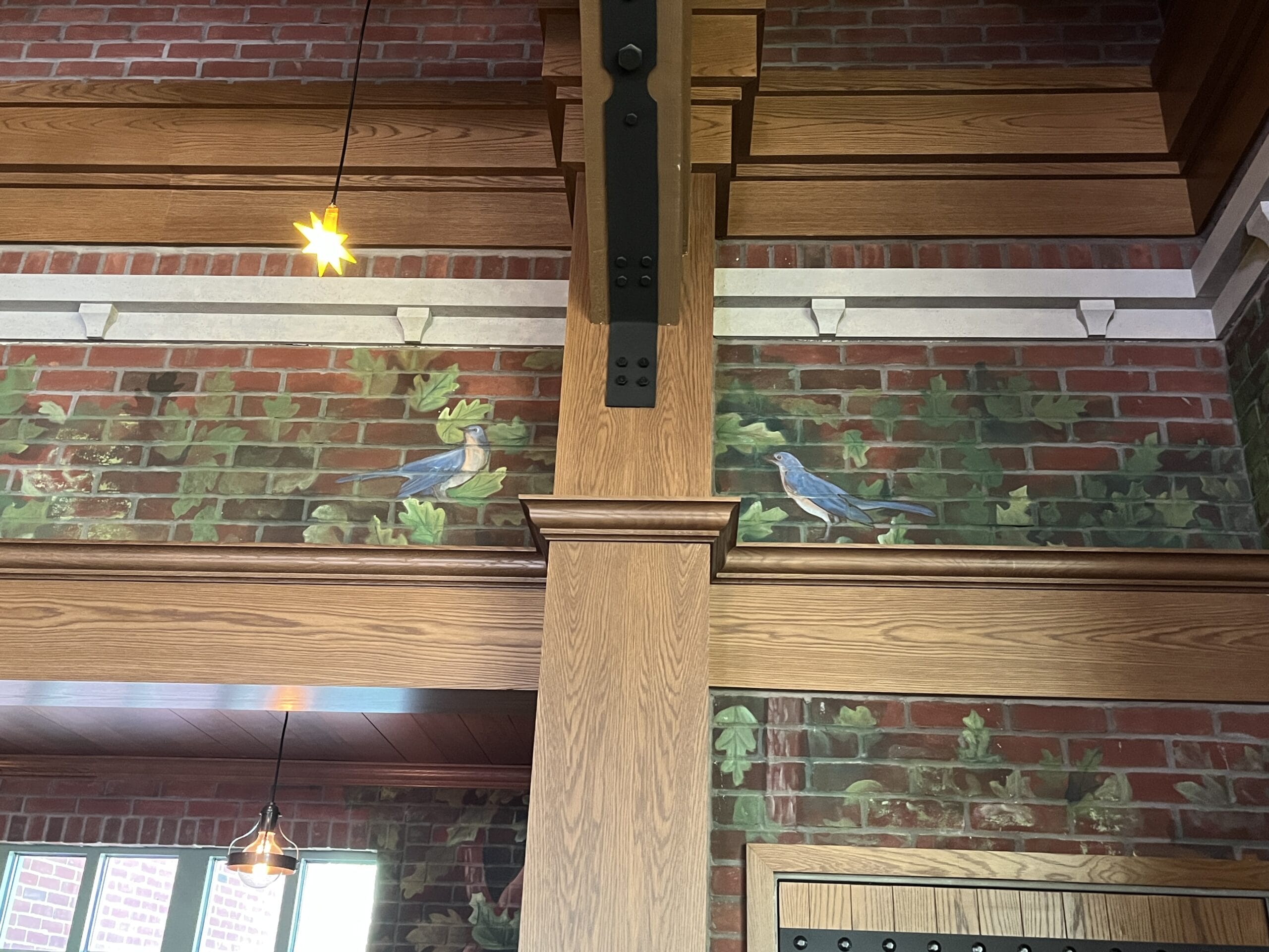Charming mural of two birds and green leaves on brick at The Oak & Star Tavern, divided by wood beams—no Disney castle seen here.