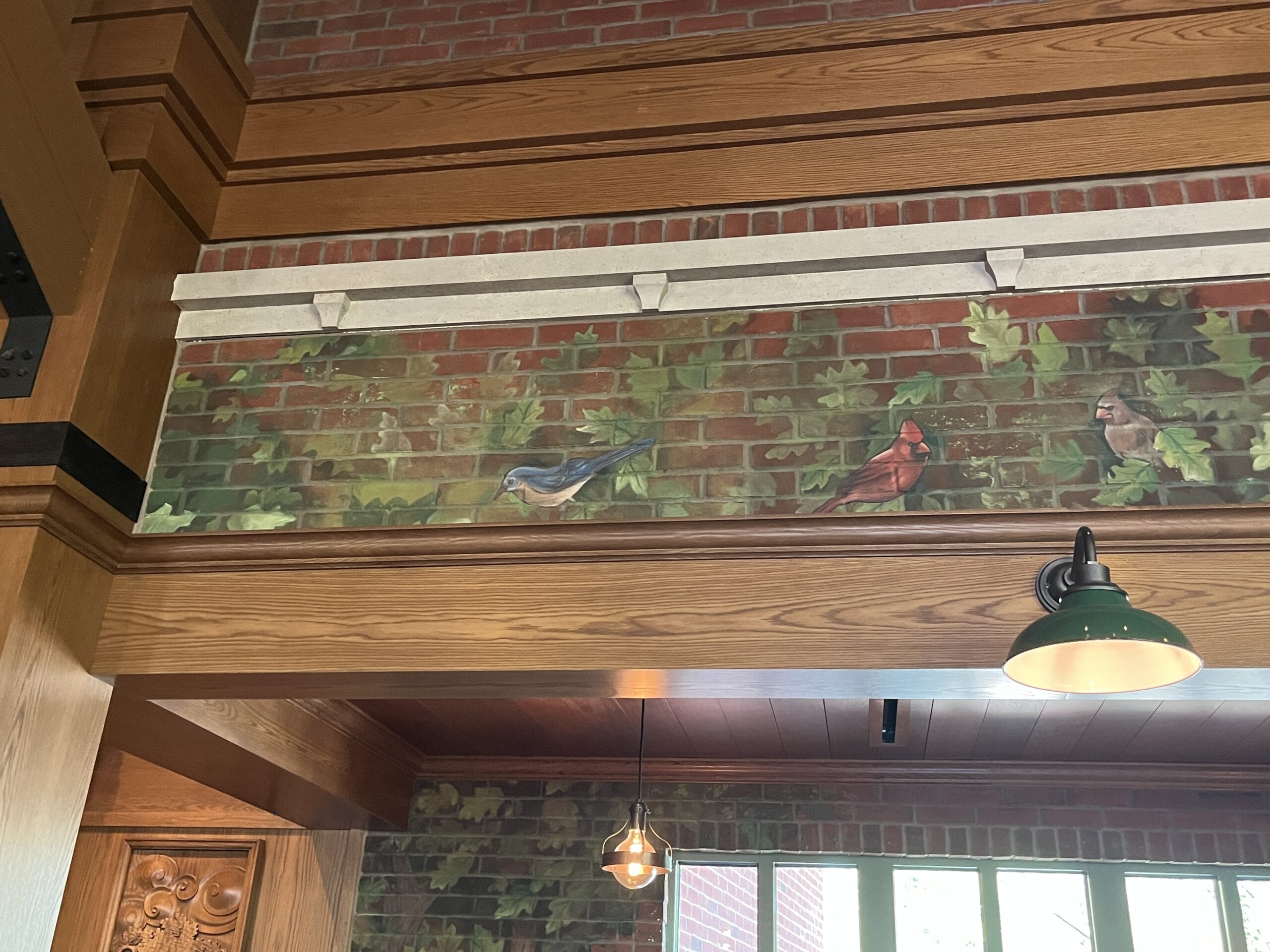 A mural of three birds on ivy-covered bricks above wood paneling at The Oak & Star Tavern, glowing green lights reminiscent of Disney’s immersive dining atmospheres.
