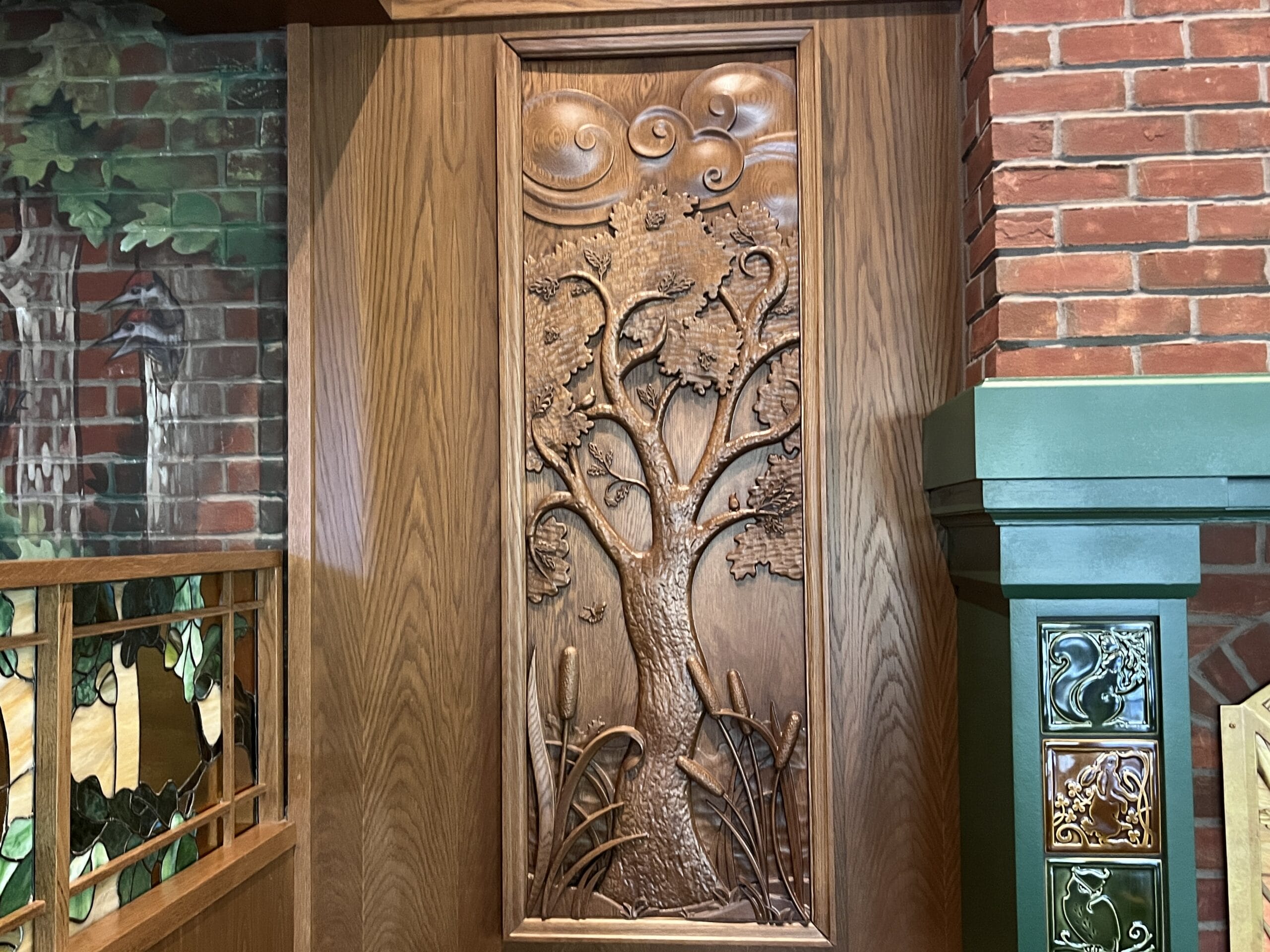 Wooden panel with carved tree and cattails at The Oak & Star Tavern, set indoors between brick and green walls—no castle like Disney’s.